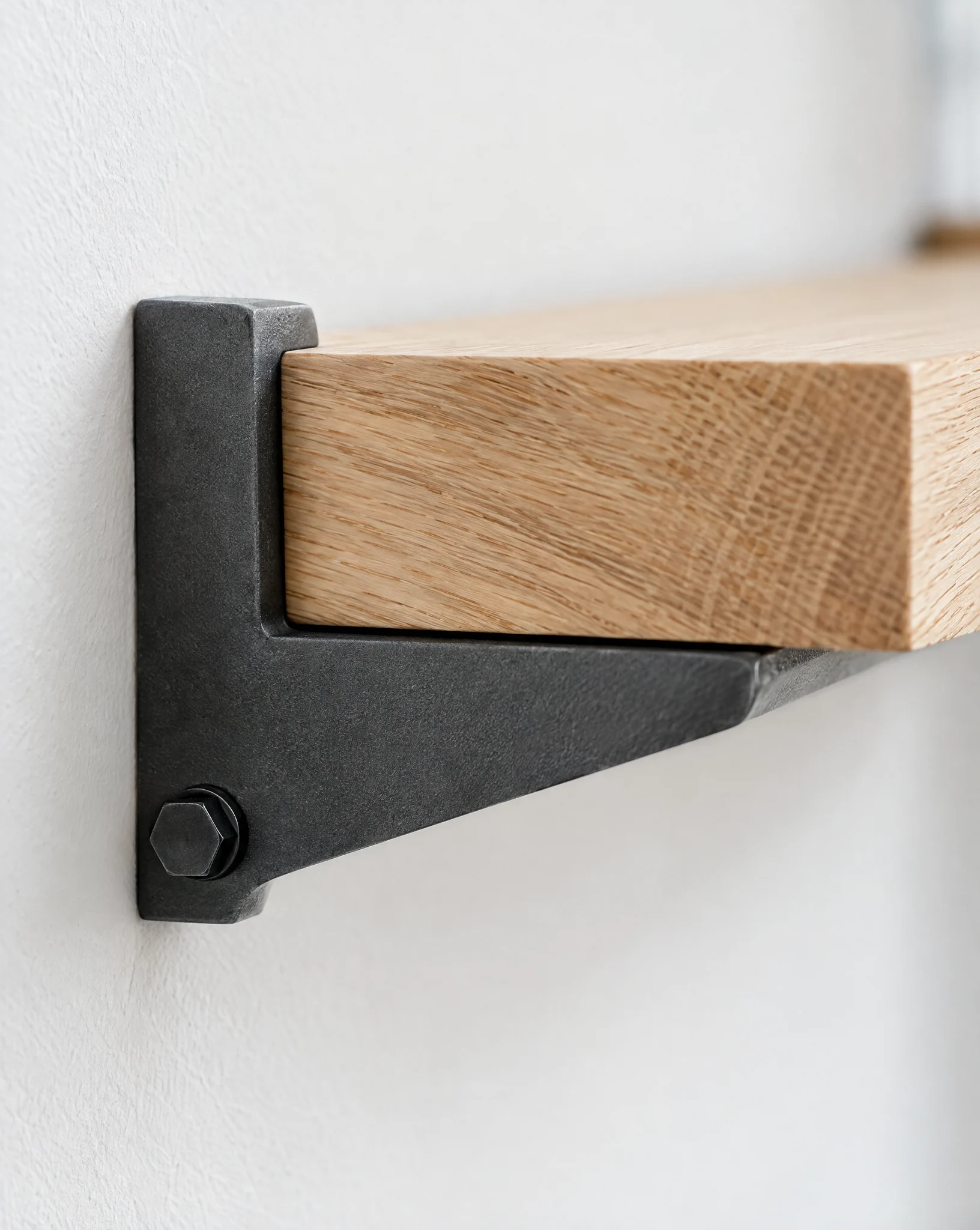 A graphite steel bracket bolted to a white wall holding the end of a solid oak shelf