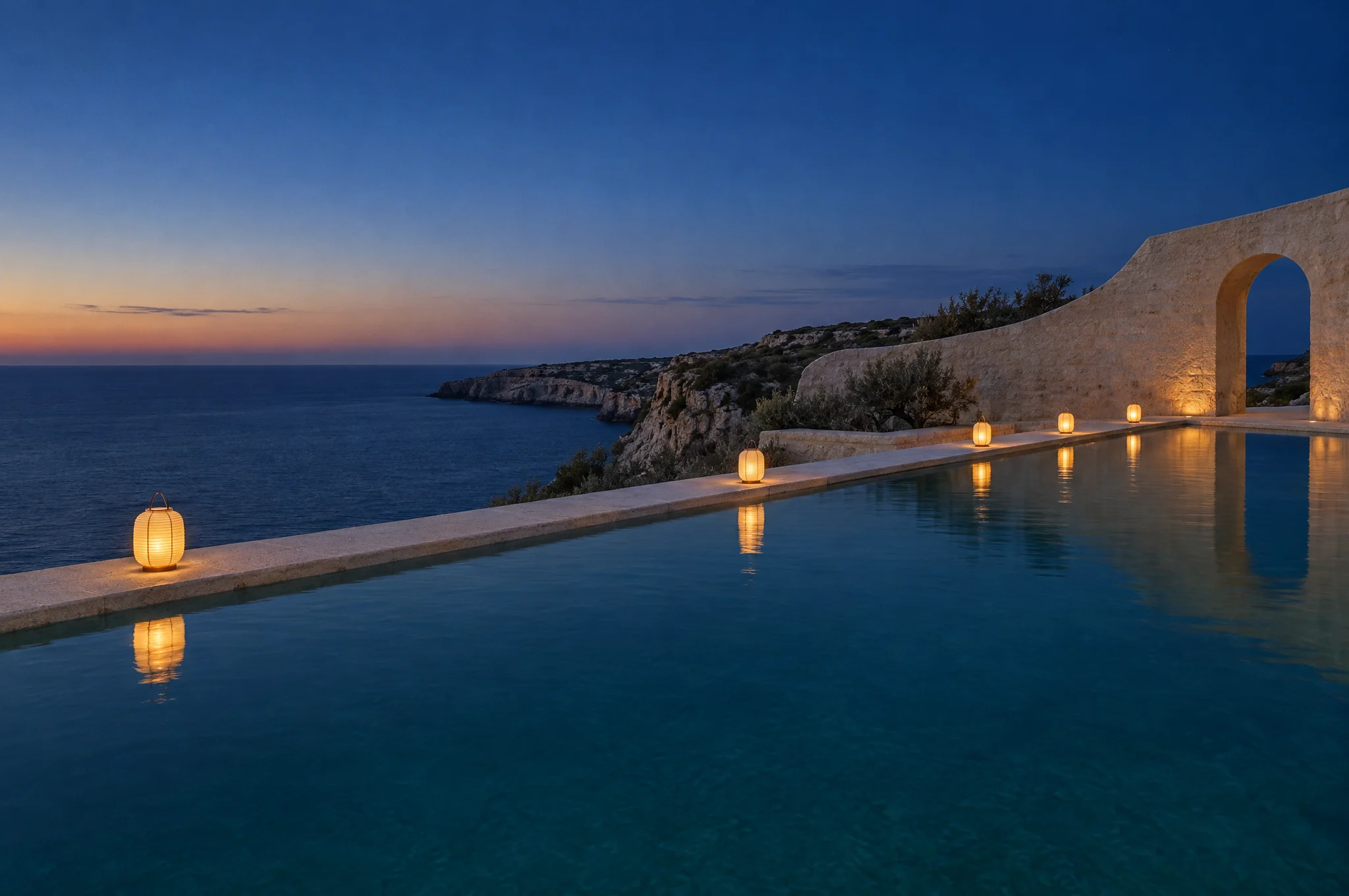 The limestone pool at blue hour, with small lanterns along its edge reflected in the still water
