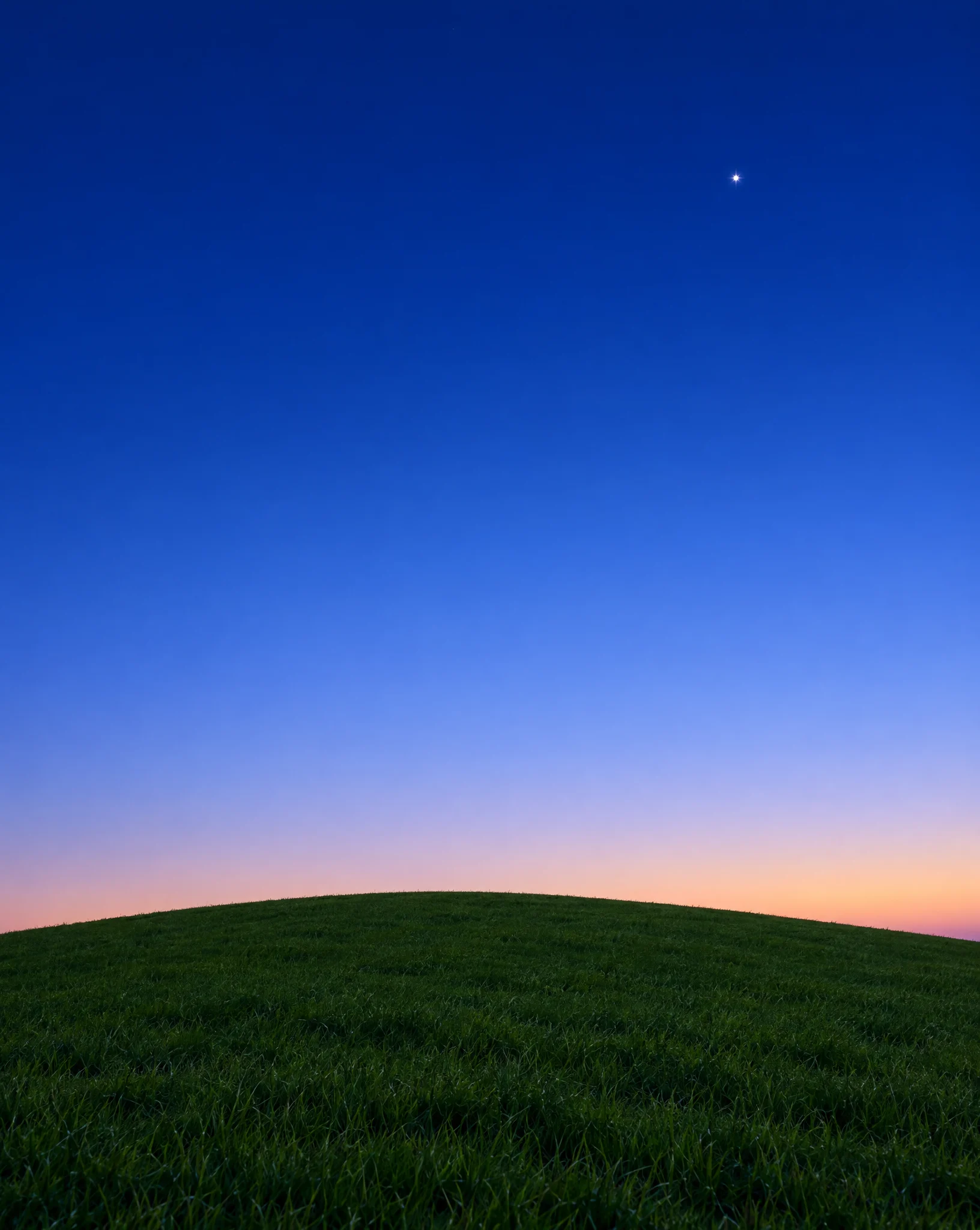The dark hill at dusk under a deep blue sky with a single bright star
