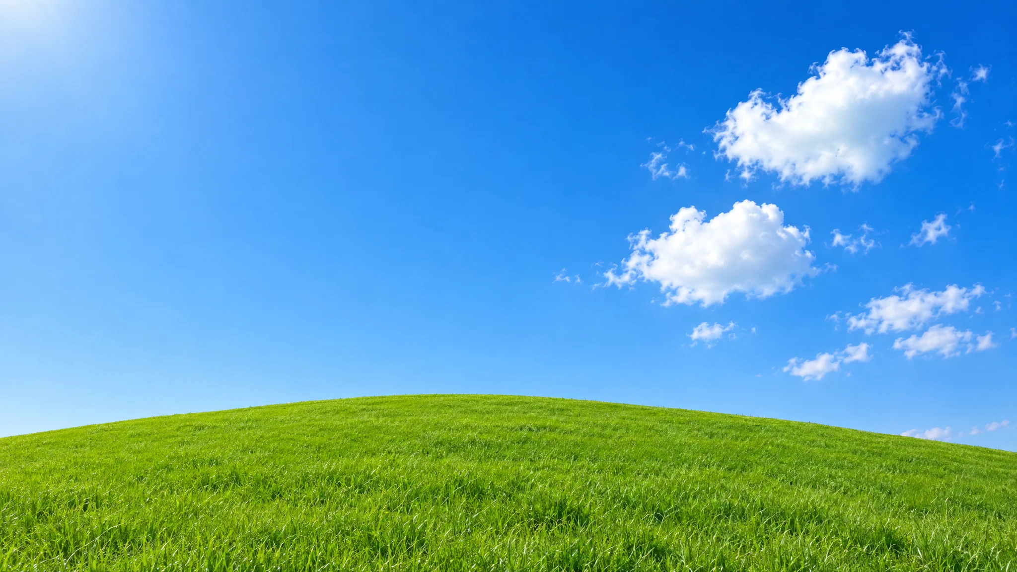 A smooth green hill under a deep blue sky with a few white clouds