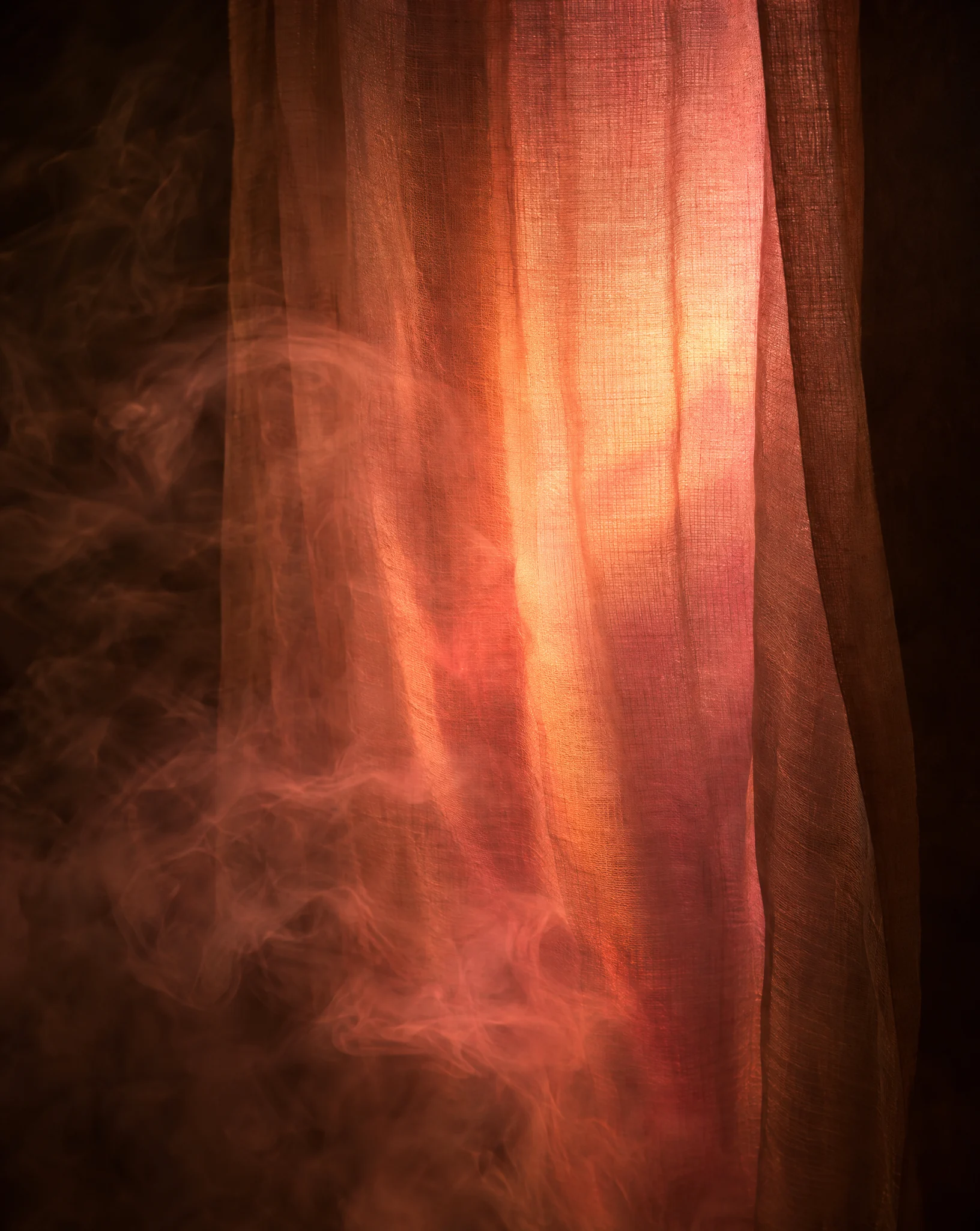 A loosely woven scrim lit from behind in apricot and rose, with mist curling in front of it