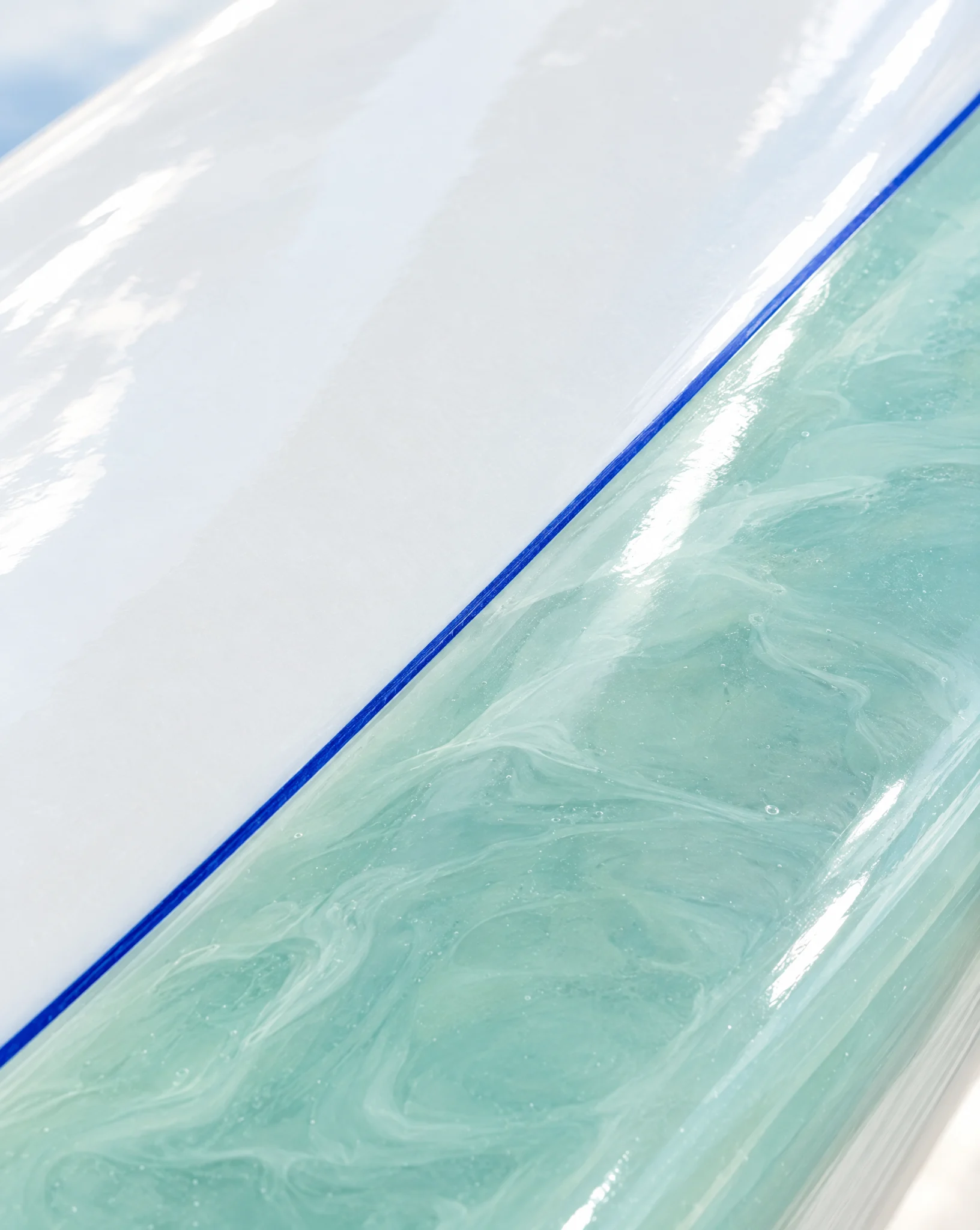 Close view of a glassy seafoam resin panel edged with a thin cobalt pinline on a white board