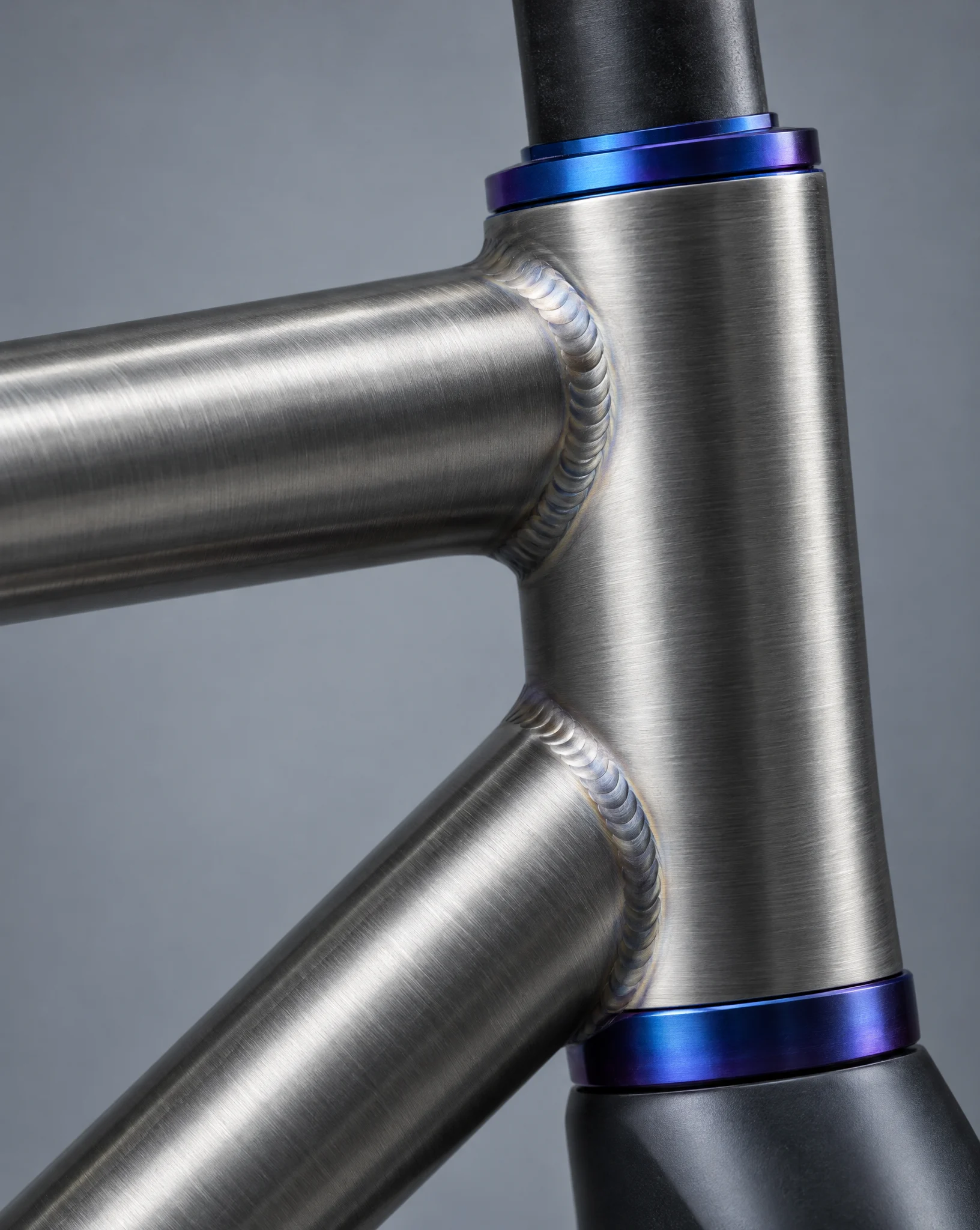 Close-up of clean hand welds joining brushed titanium tubes at a blue-violet anodized head tube