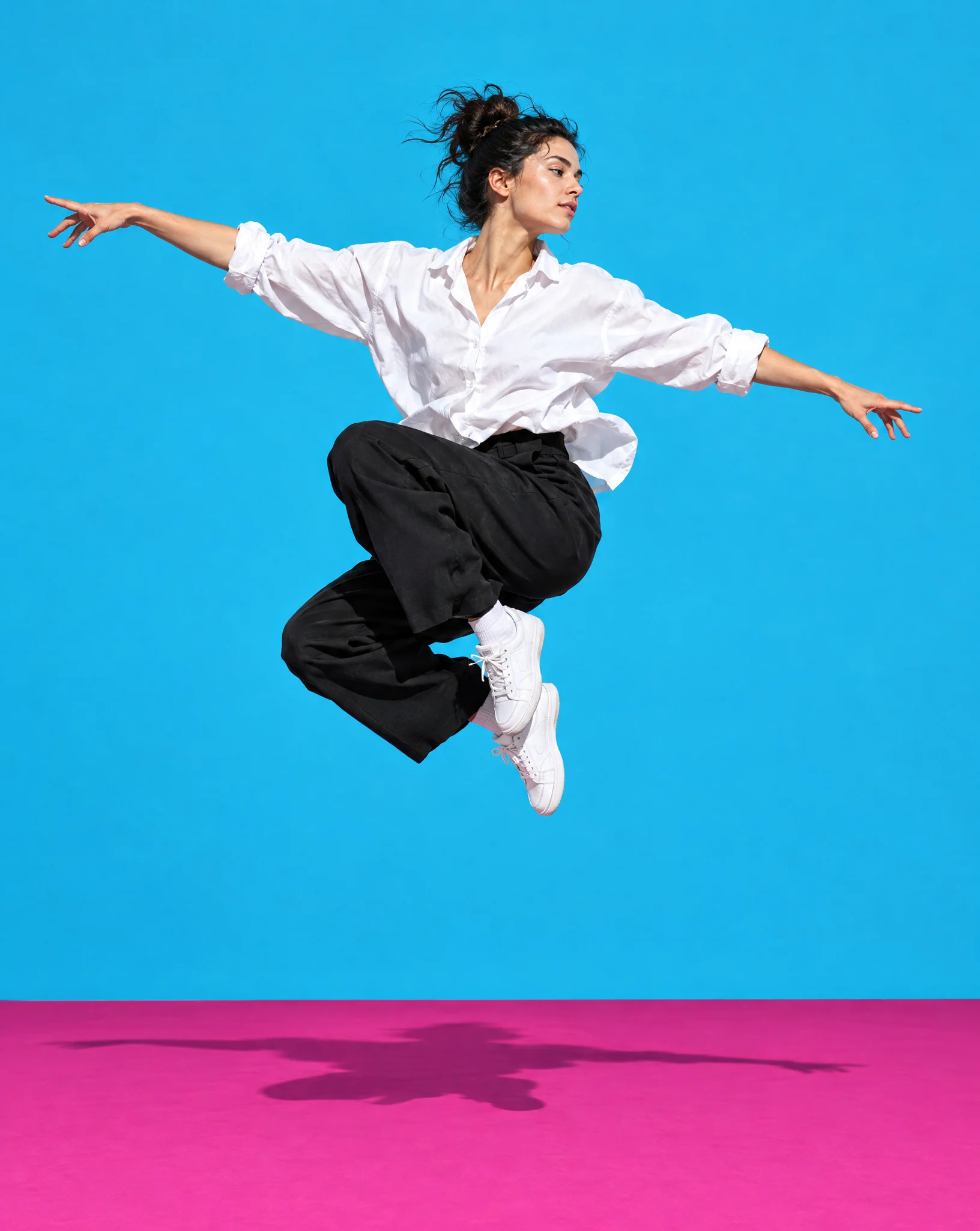 A dancer in a white shirt and black trousers mid-jump against a cyan wall above a magenta floor