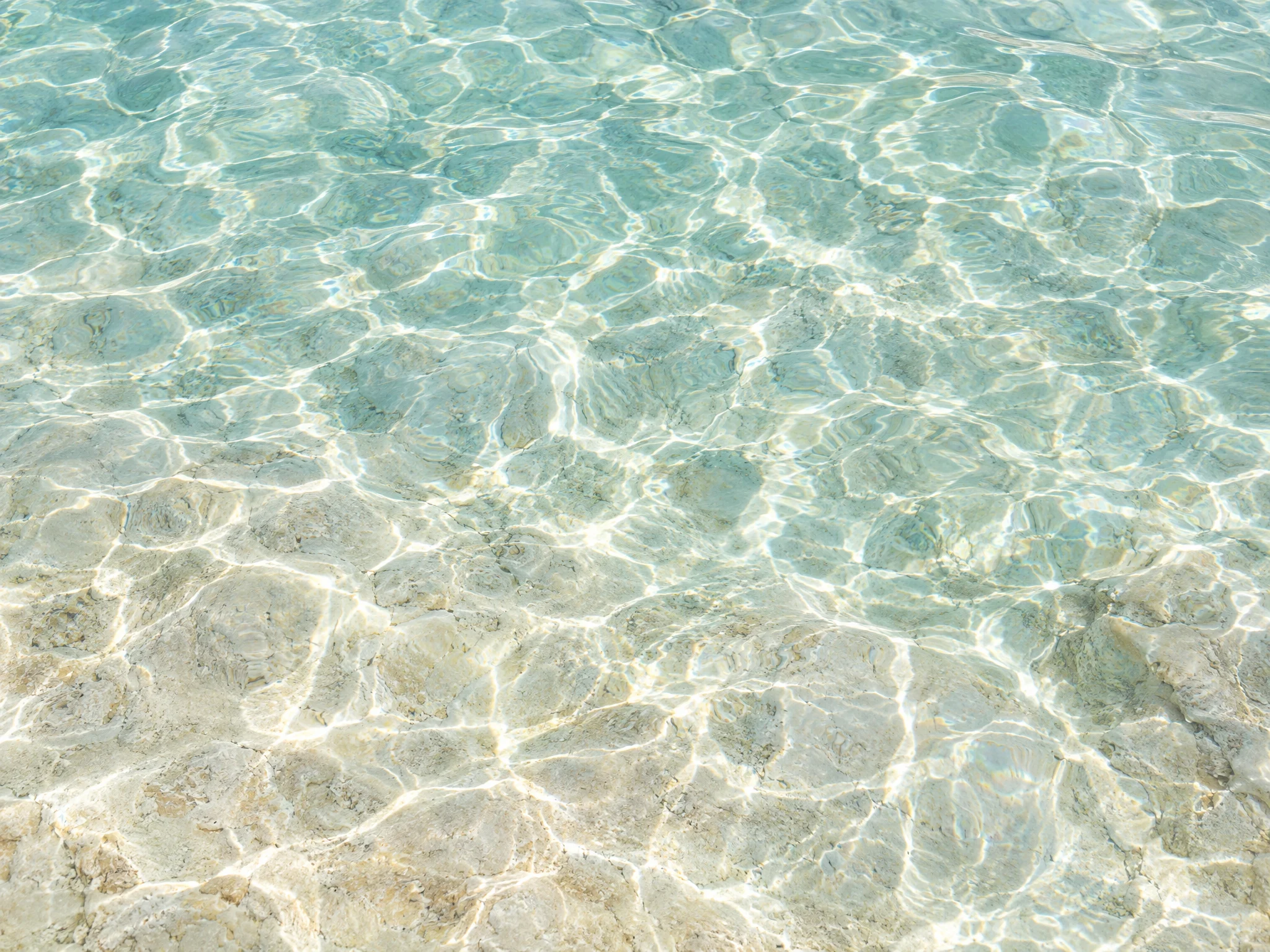Sunlight caustics rippling over a pale limestone pool floor