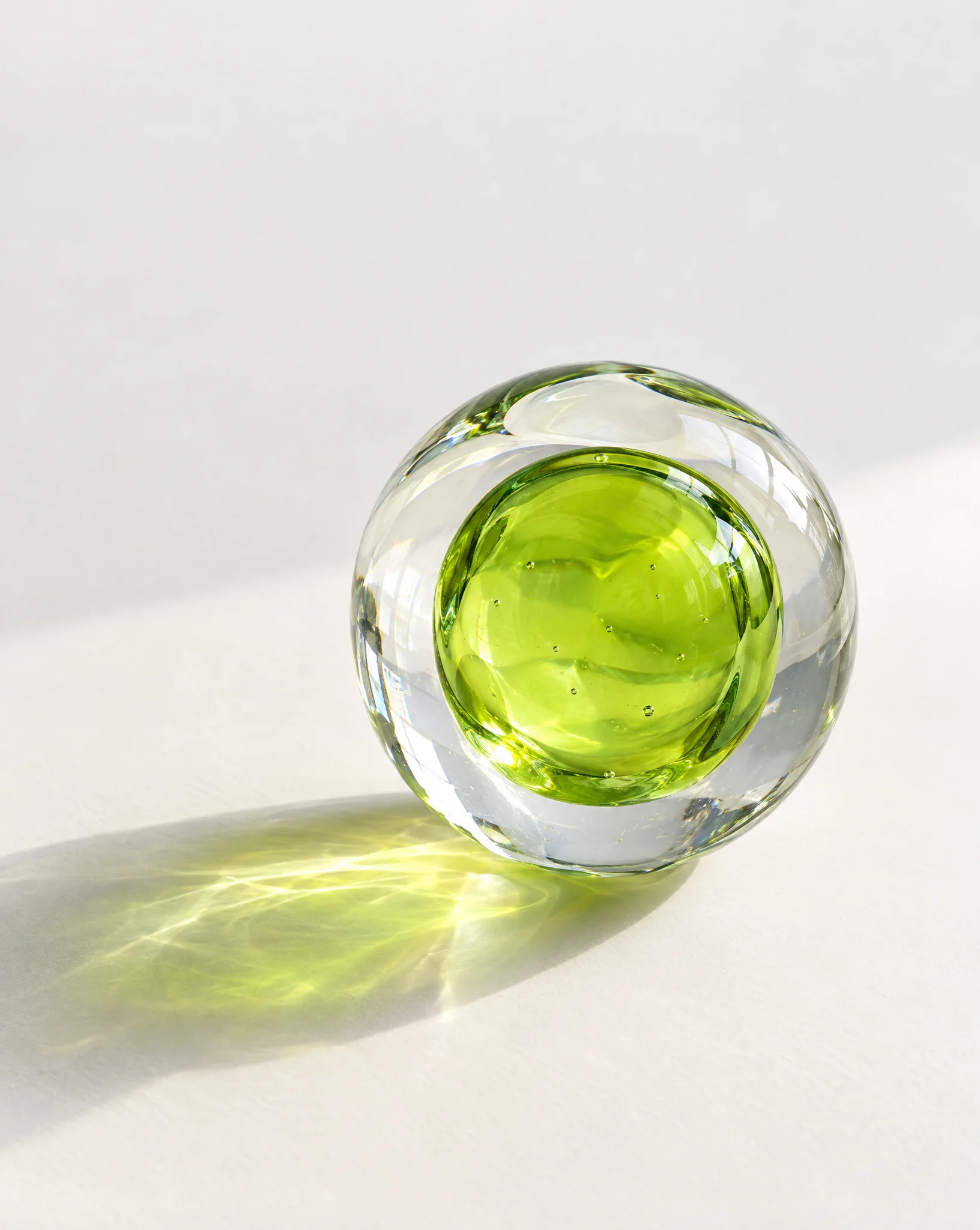 A clear glass orb with a bright lime core casting green light across a white surface
