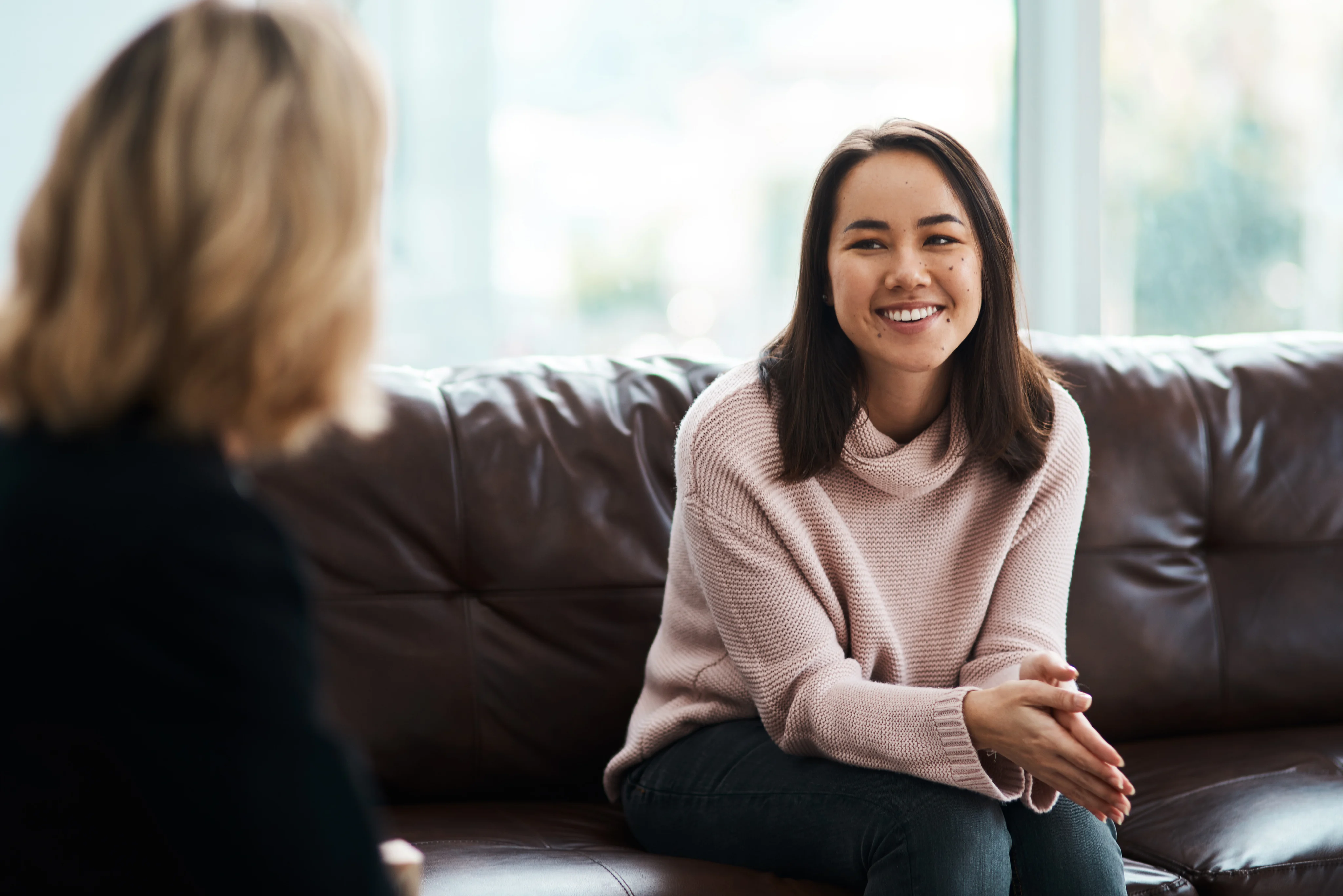 A smiling woman in a pink sweater talking with another woman seated opposite her