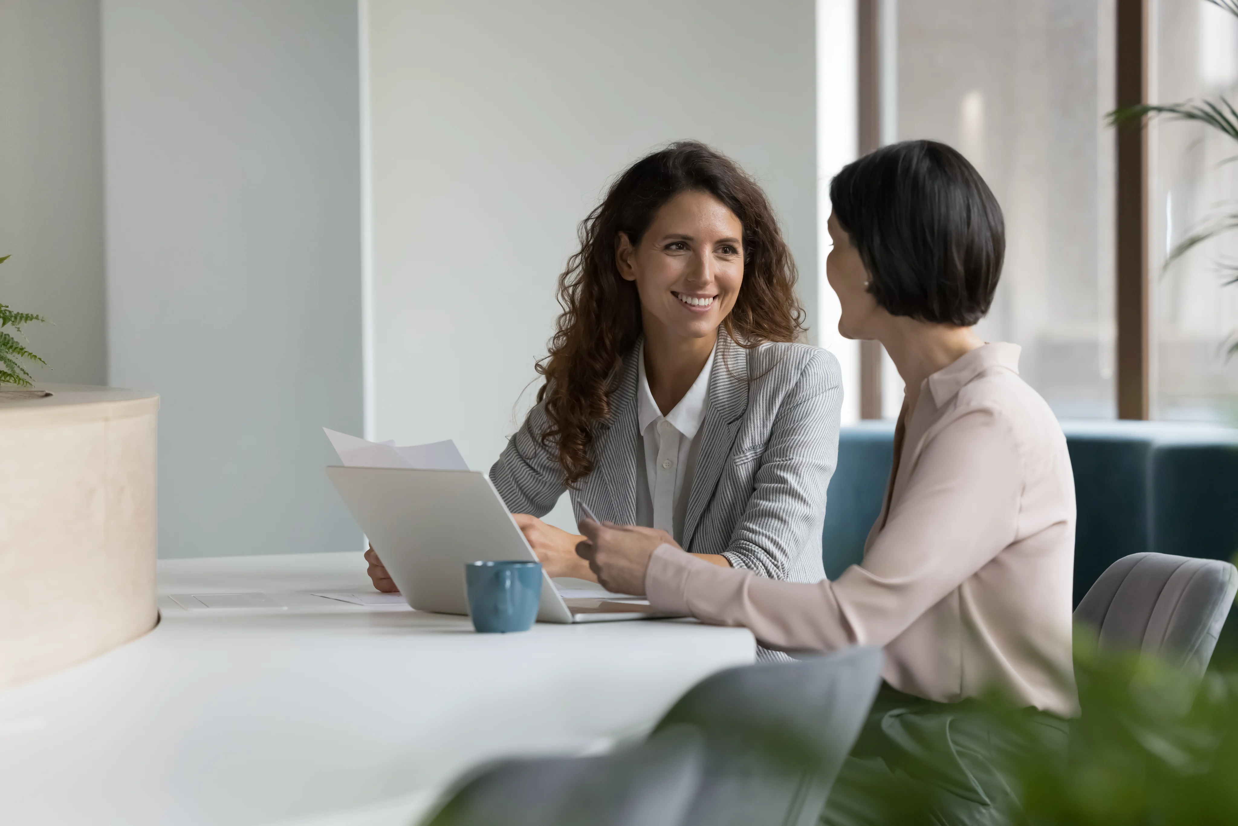 Two women reviewing documents together at a table with a laptop