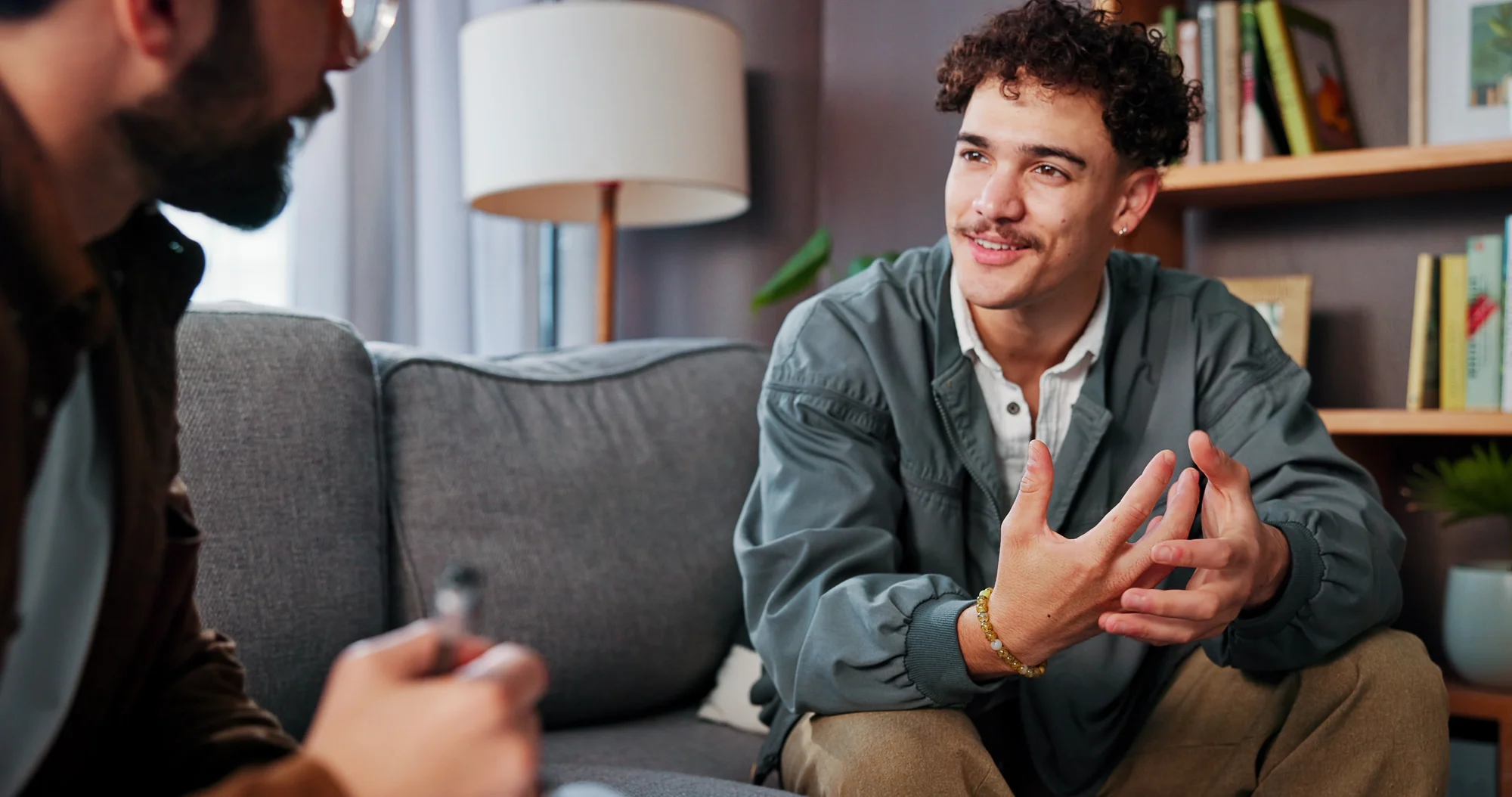 Two adult men sharing a conversation on a sofa. Representative care imagery.