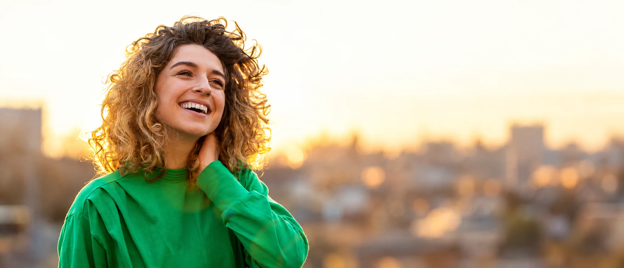 A smiling woman outdoors at sunset, looking up with hope and renewed wellbeing