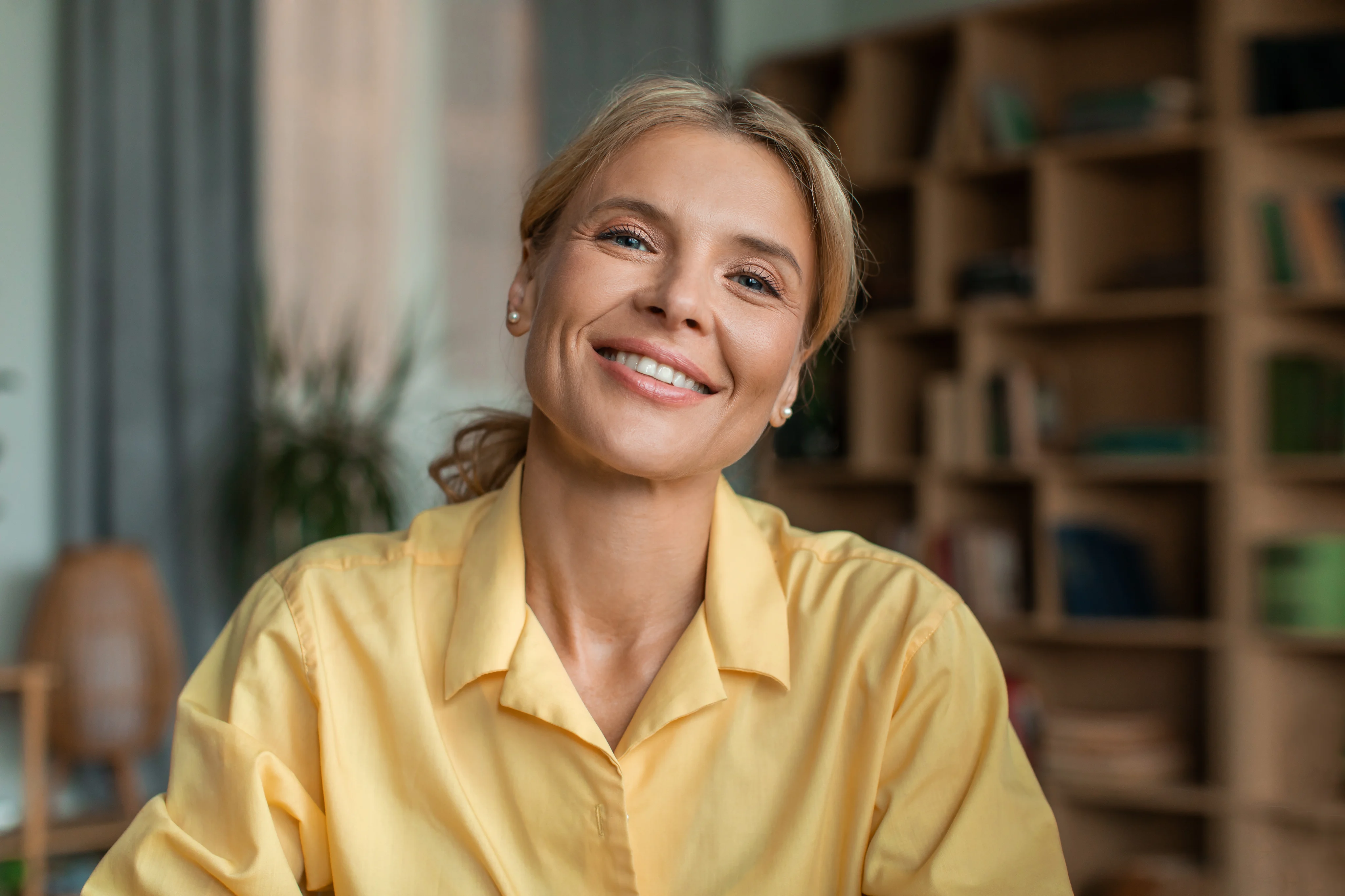 A smiling woman in a yellow shirt in a bright home or office