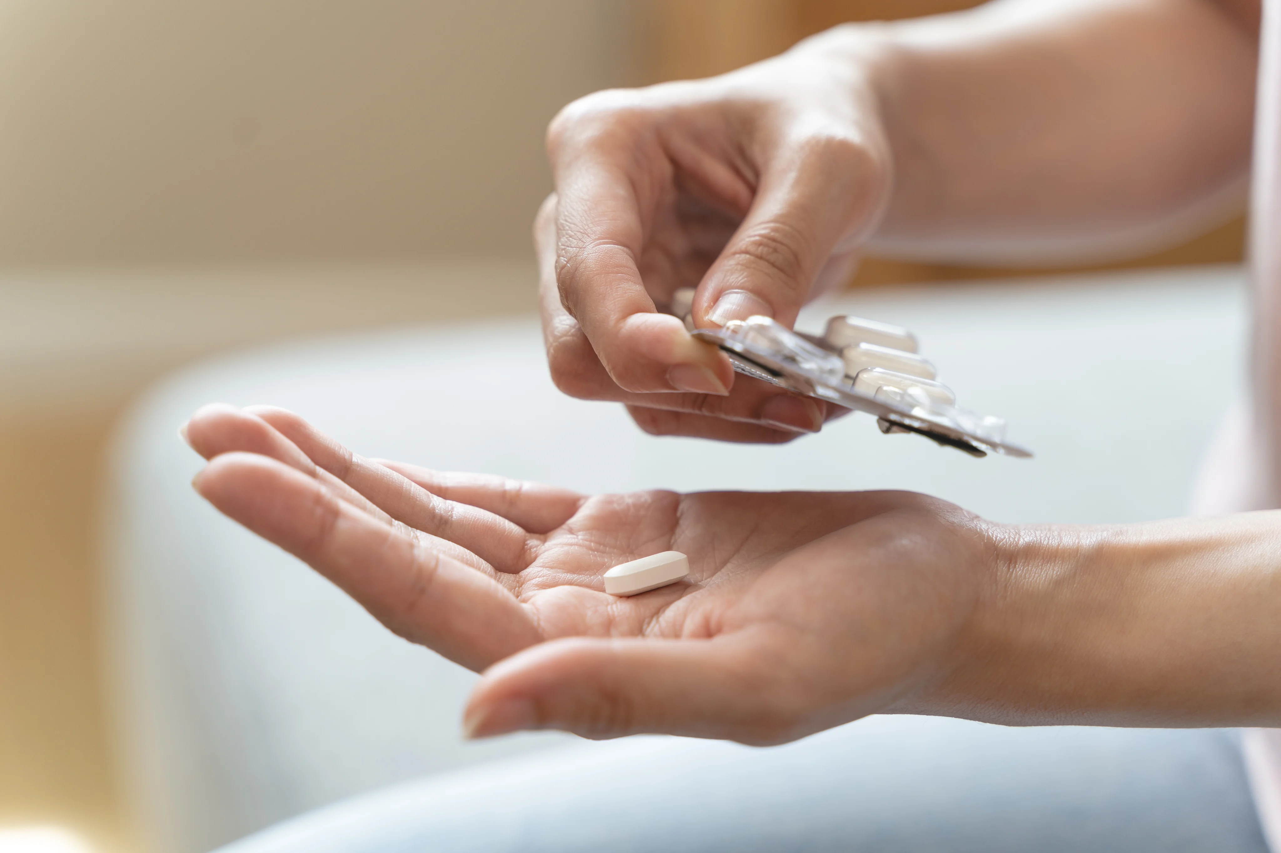 Hands holding a blister pack above a white tablet resting in an open palm