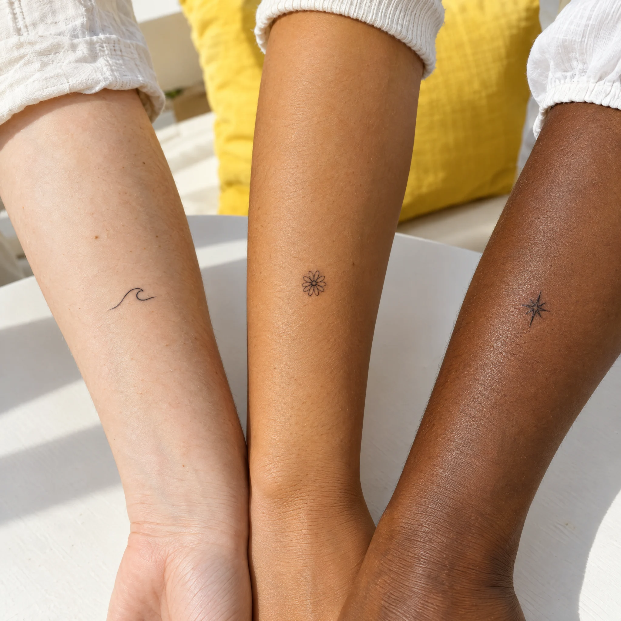 Three friends' forearms wearing a tiny wave, daisy and star temporary tattoo