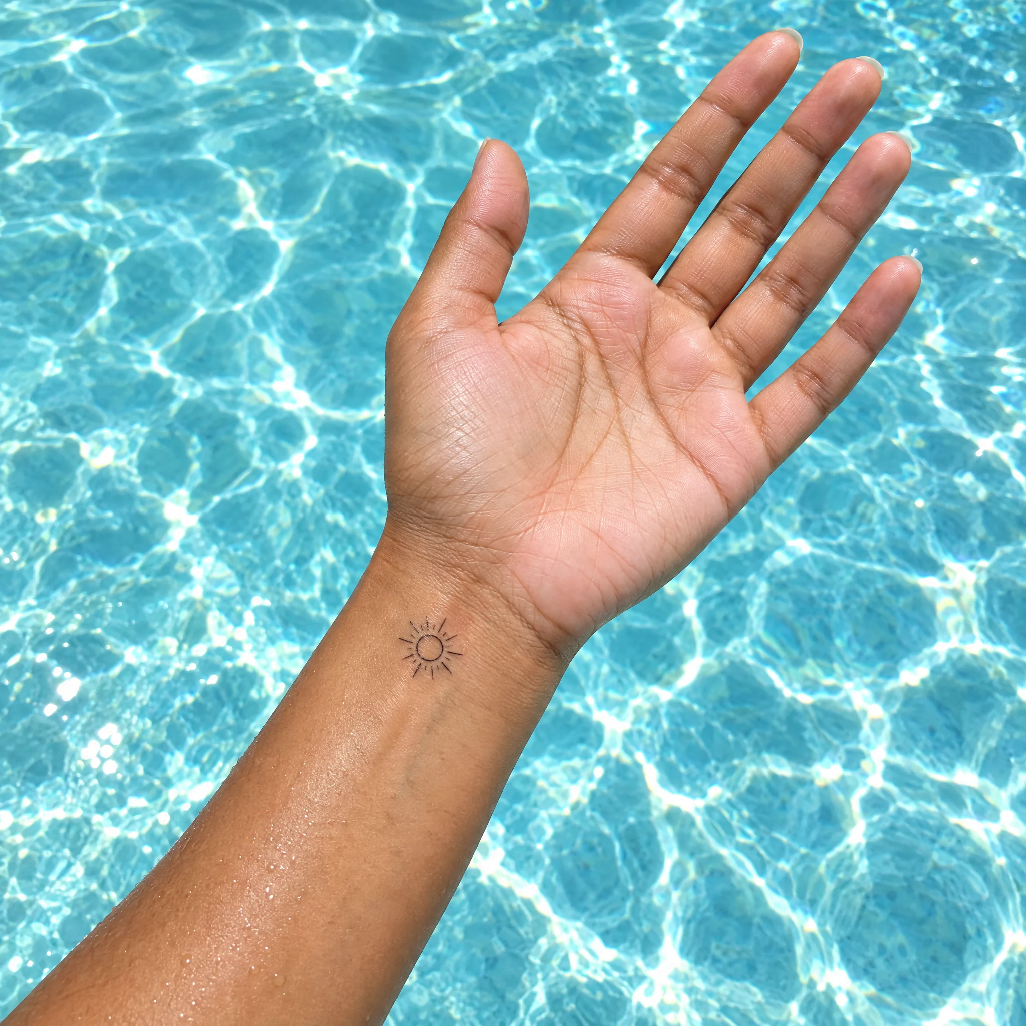Small sun temporary tattoo on an inner wrist held over pool water