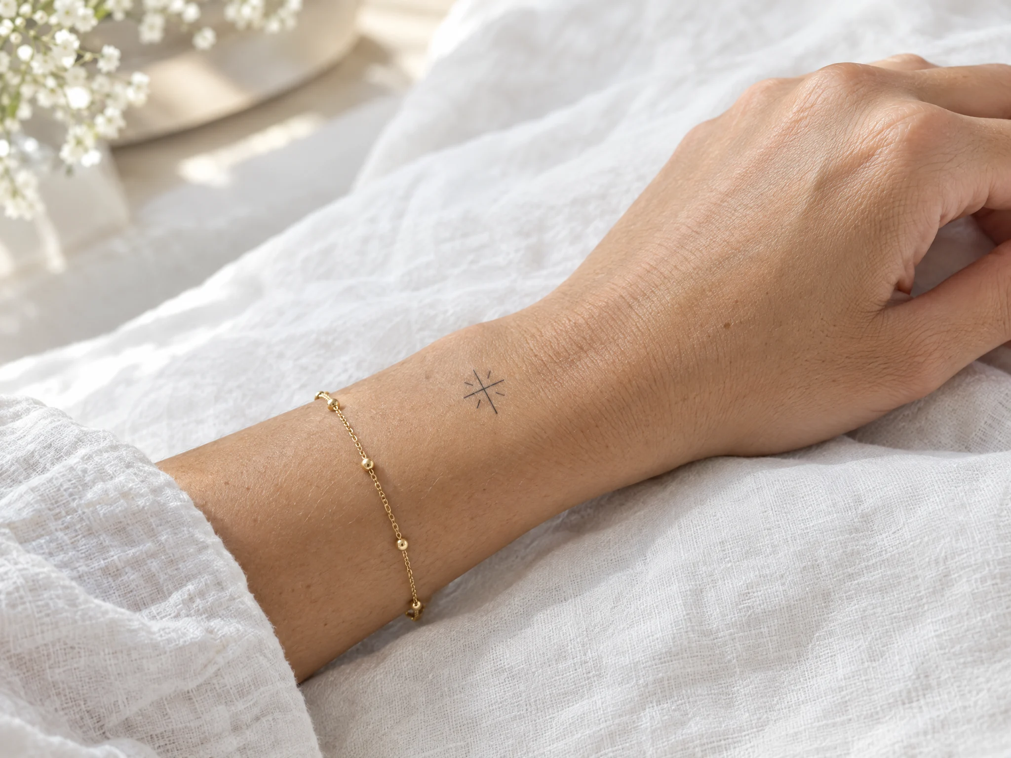 Tiny fine-line cross temporary tattoo on a wrist beside a gold bracelet