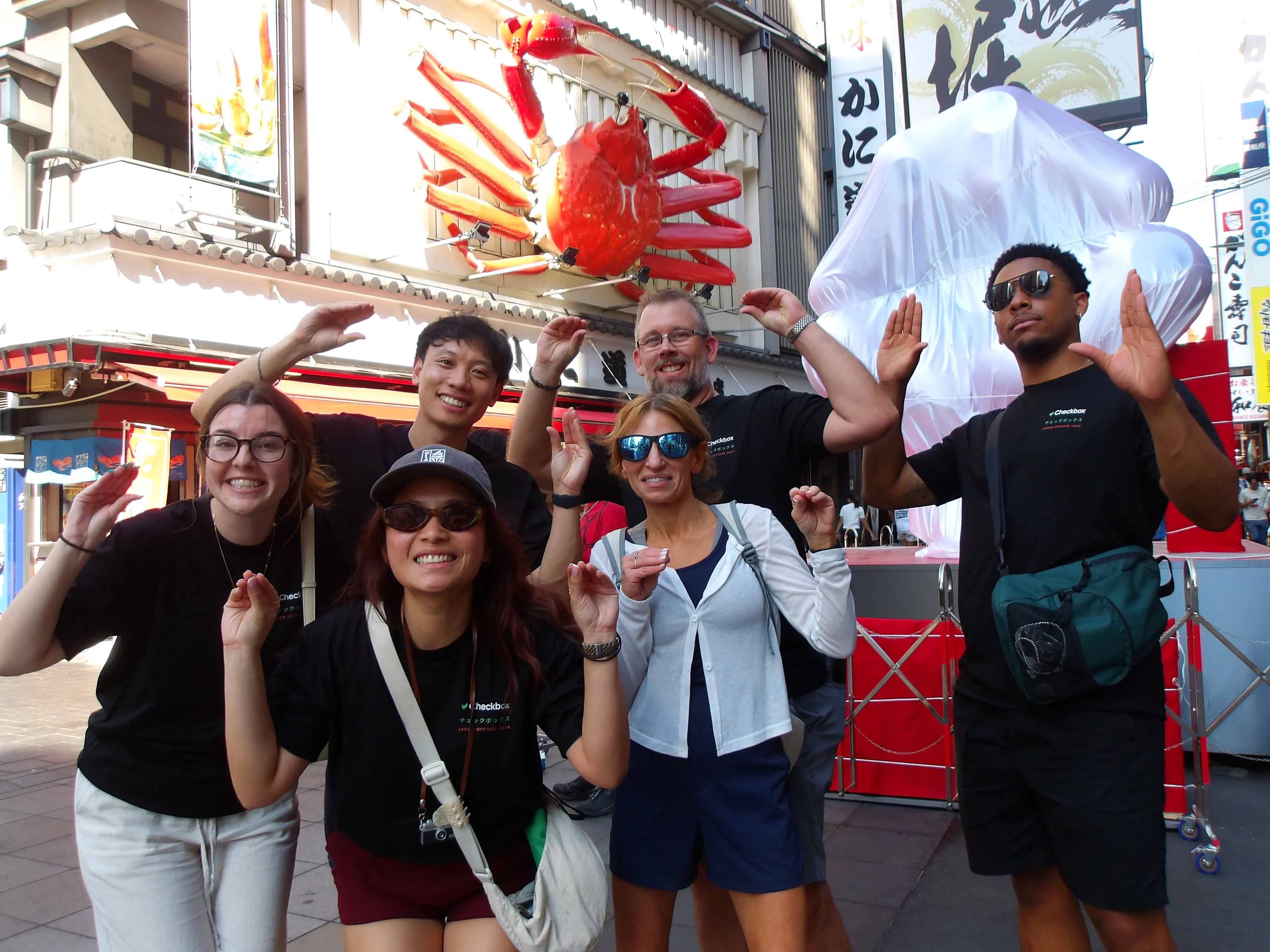 Checkbox teammates posing together beneath a giant crab sign in Japan