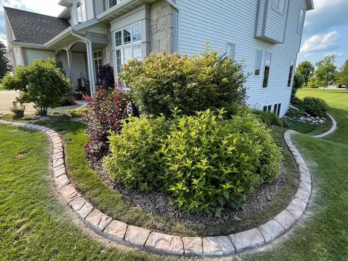 Curved stamped concrete garden border around shrubs and a rock bed in front of a home