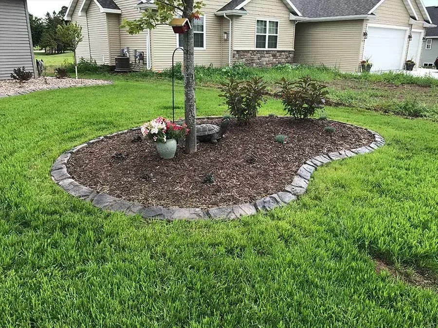 Stamped concrete curbing around a mulched tree bed beside a home