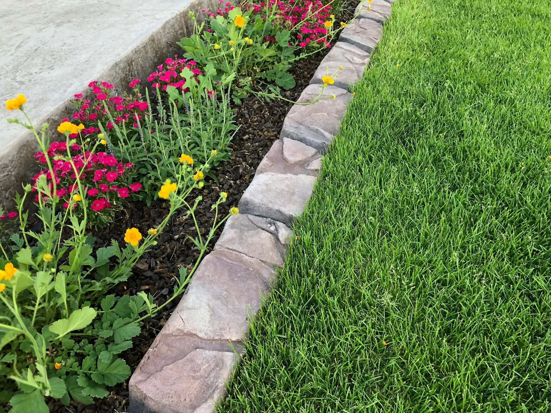 Stone-textured concrete curbing separating colorful flowers from a green lawn