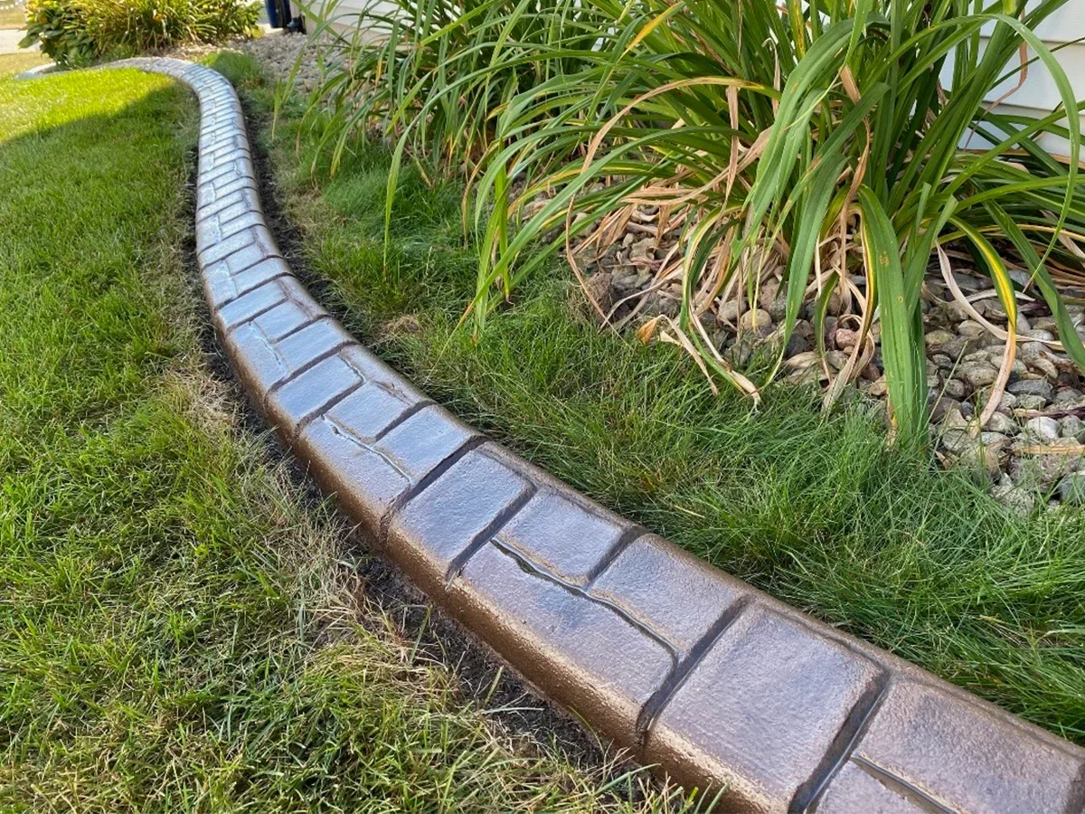 Brick-pattern concrete curbing between a lawn and ornamental grasses