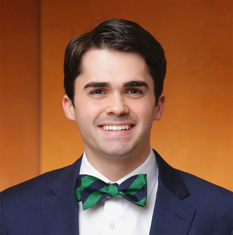 A smiling young man in a navy suit and a green and blue striped bow tie, exuding confidence in a digital product environment.