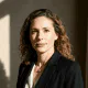 A confident woman with curly brown hair and a dark blazer, looking directly, embodying expertise in digital product.