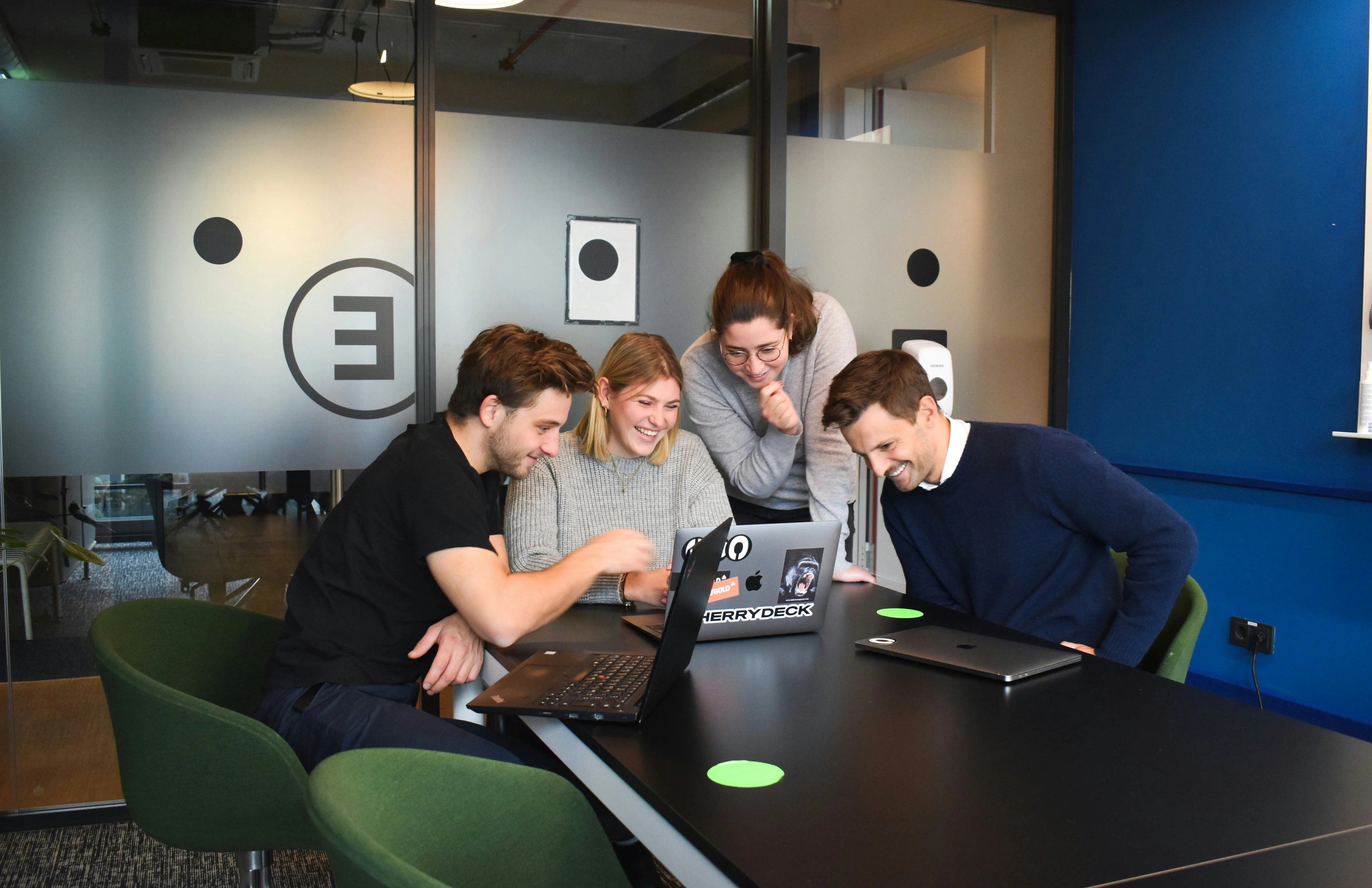 Office team collaborating around laptops in a glass-walled meeting room