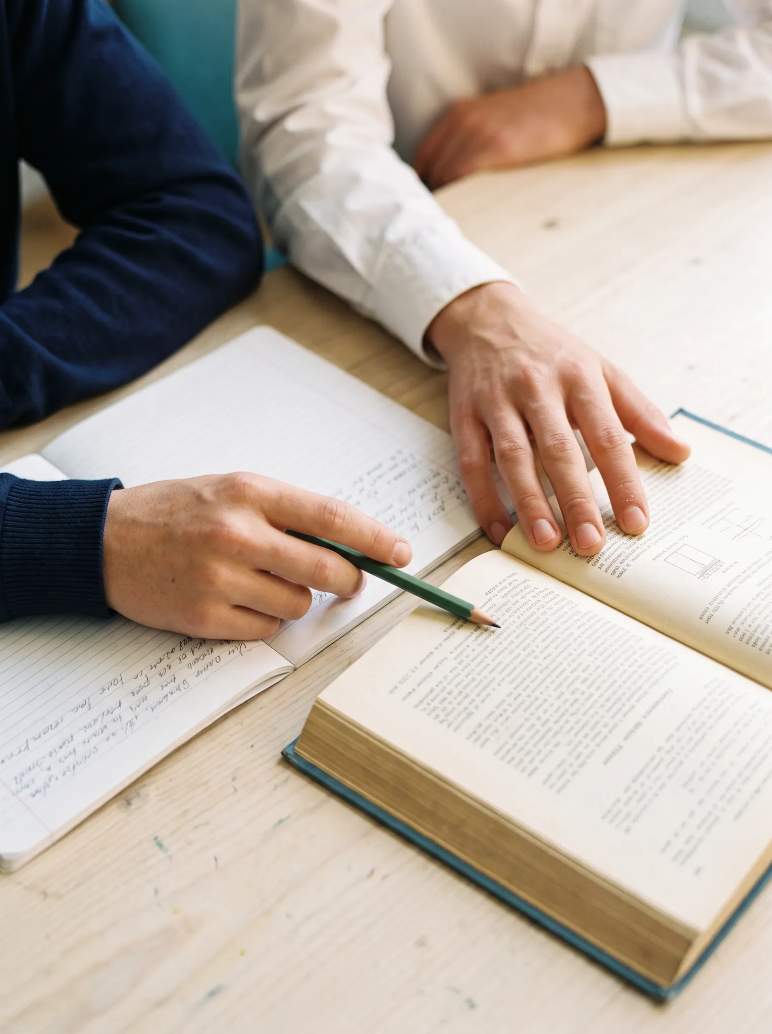 Illustrative study scene with hands working together over a book and notebook