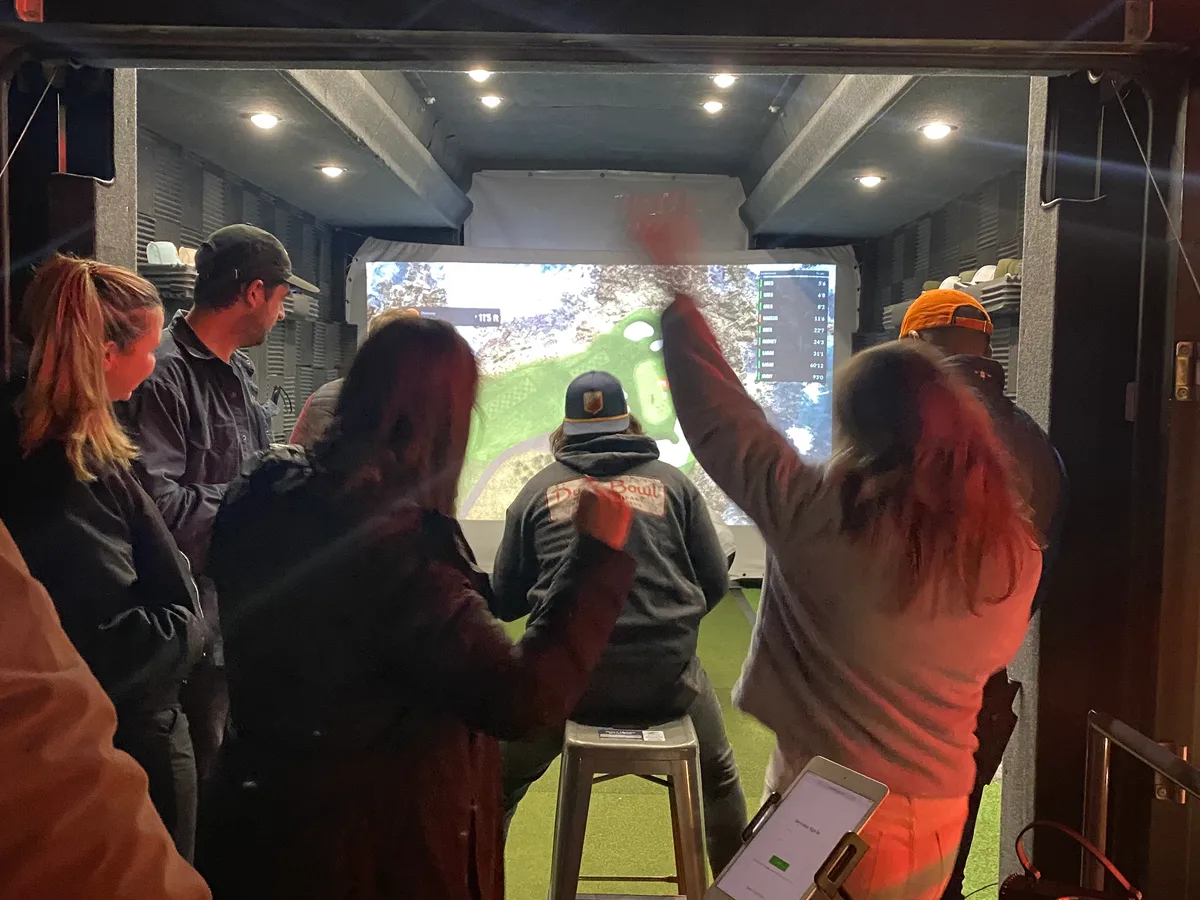 Group of friends cheering inside the Dryvebox trailer as a player takes a shot on the TrackMan simulator