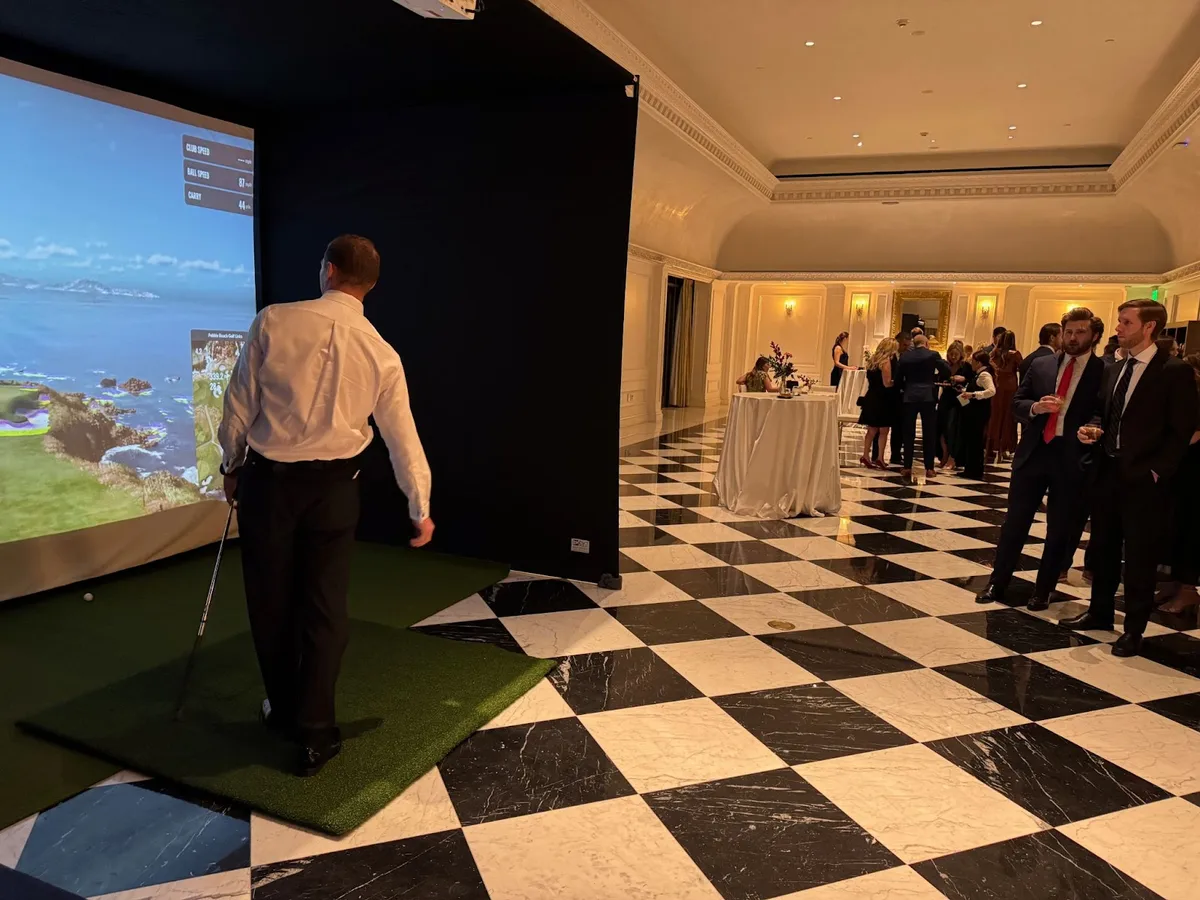 Guest hitting a Dryvebox indoor pop-up golf simulator during a hotel ballroom reception