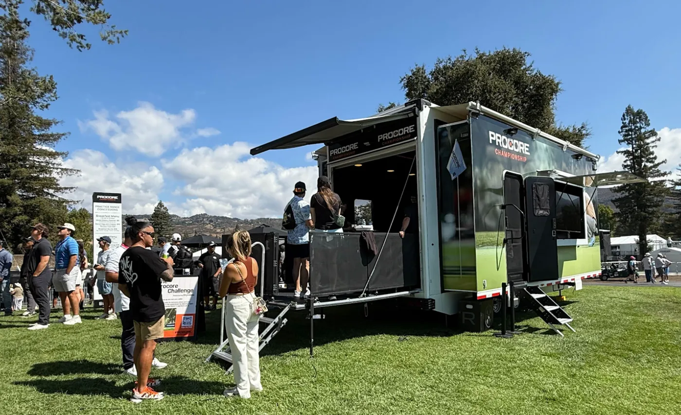 Procore Championship-wrapped Dryvebox trailer on the course with fans gathered at the party deck