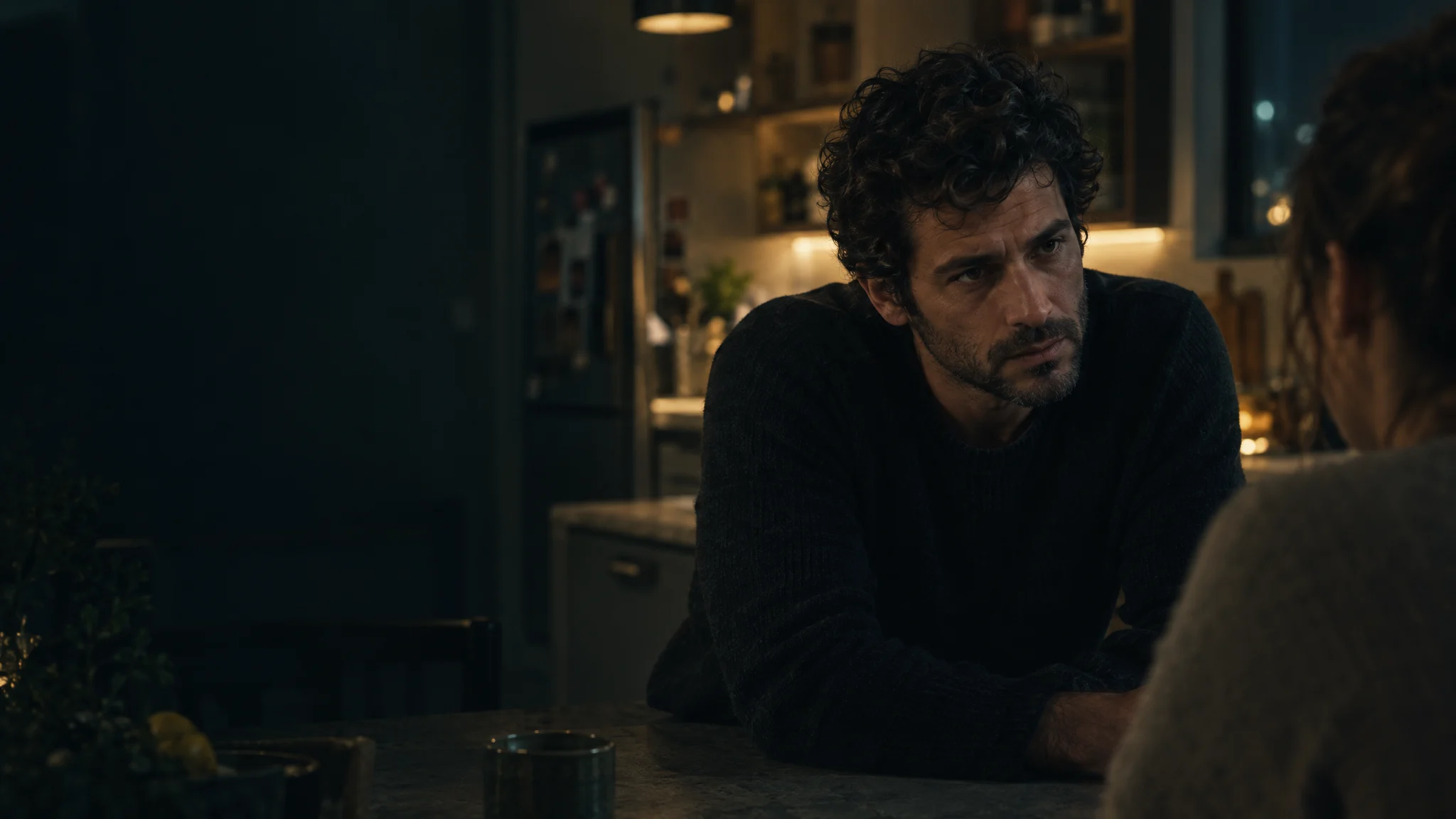 A scene from an Israeli TV drama: a man leans across a kitchen counter, talking to a woman at night.