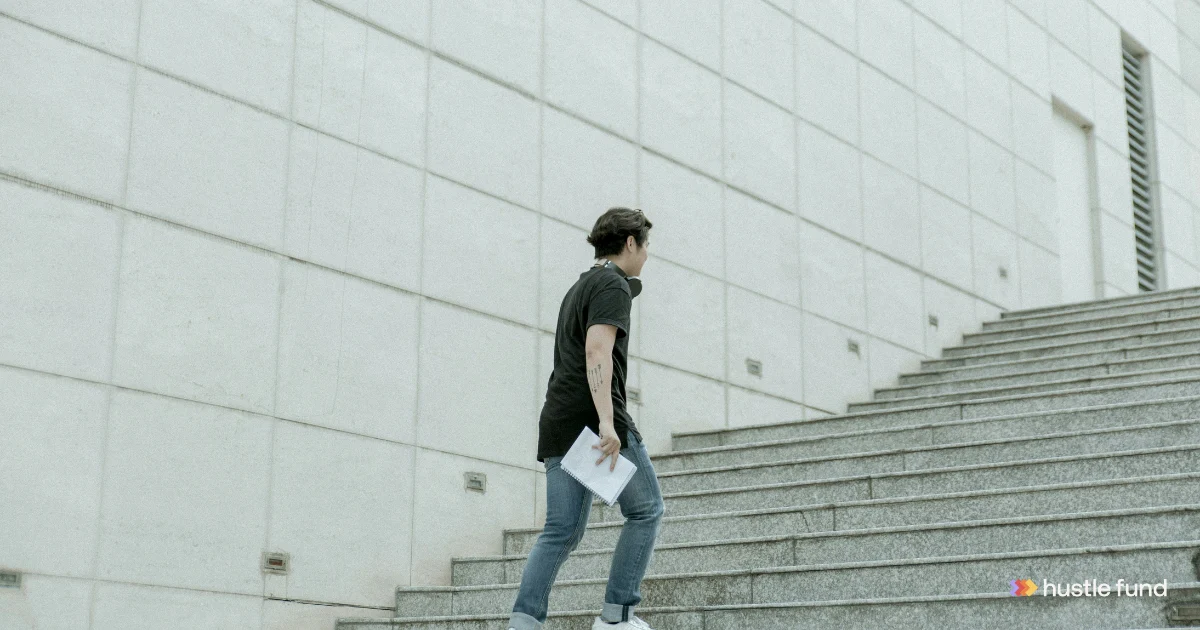 A founder carrying a notebook walks up a long concrete staircase