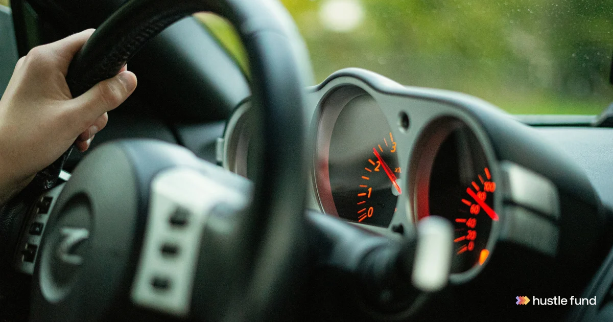 Driver holding a steering wheel with a Hustle Fund logo at the lower right