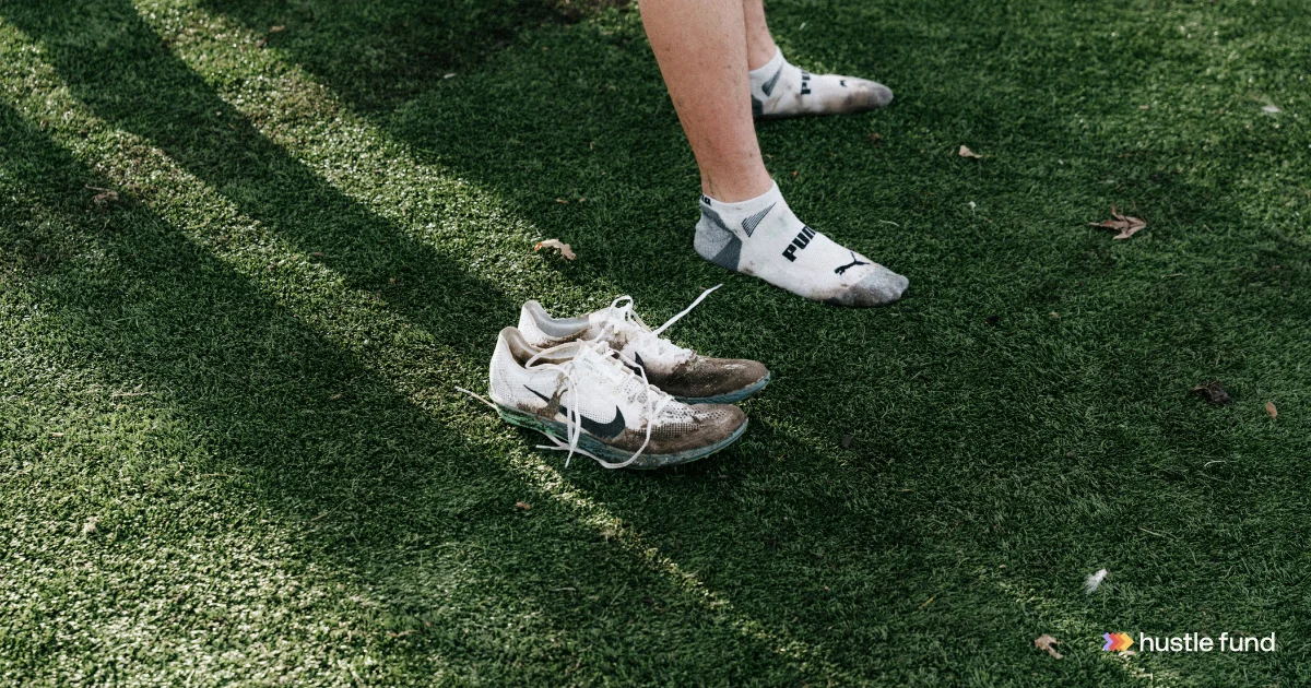 A runner standing in socks beside a pair of running shoes on grass