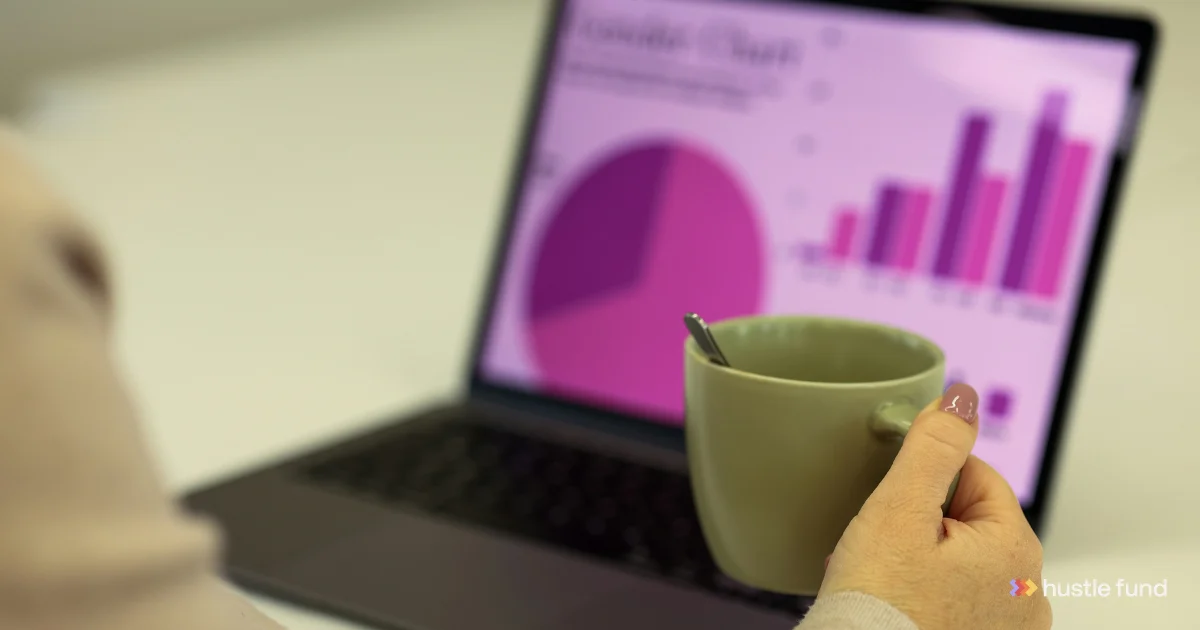 A person holding a mug in front of a laptop displaying revenue charts