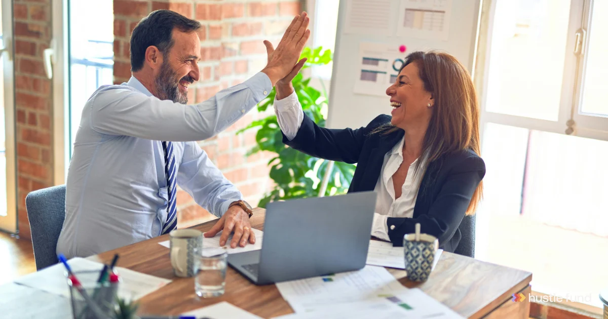 Two colleagues high-fiving across a table during a team meeting