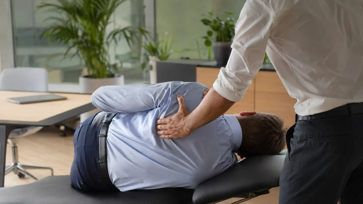 Un praticien place ses mains sur le dos d’une personne allongée sur une table de soin dans un bureau lumineux