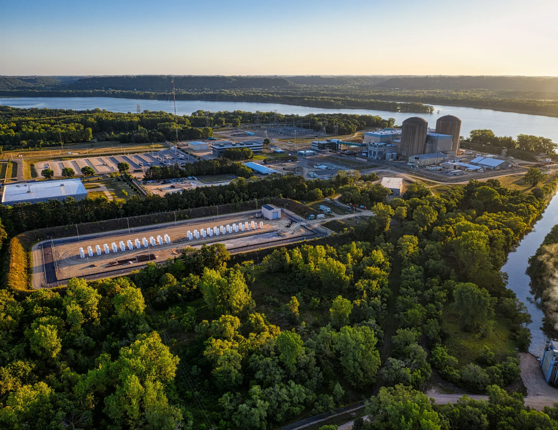 Illustrative aerial view of a riverside power facility and wooded surroundings