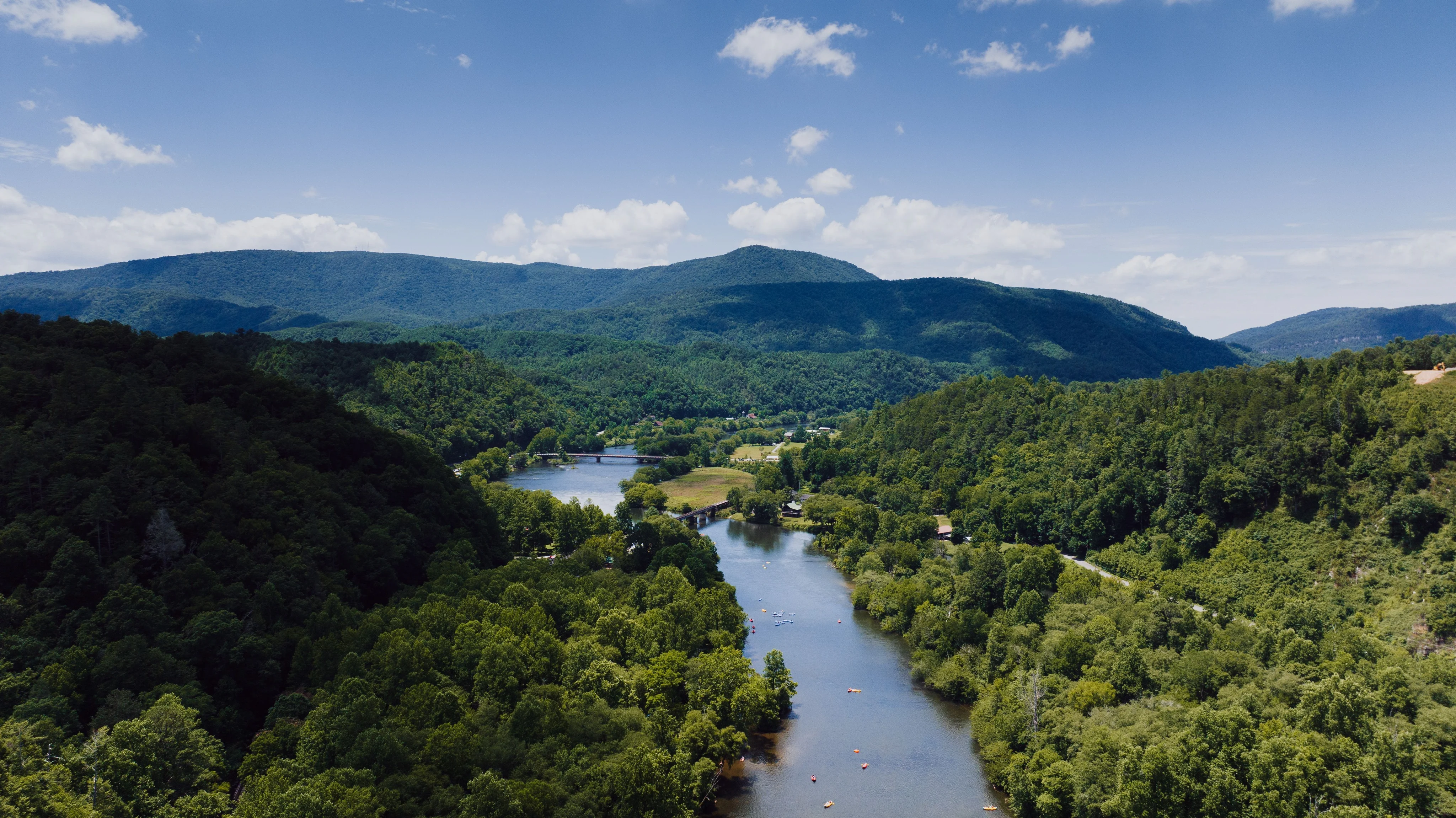 Aerial view of a wooded river valley and distant hills beneath a blue sky