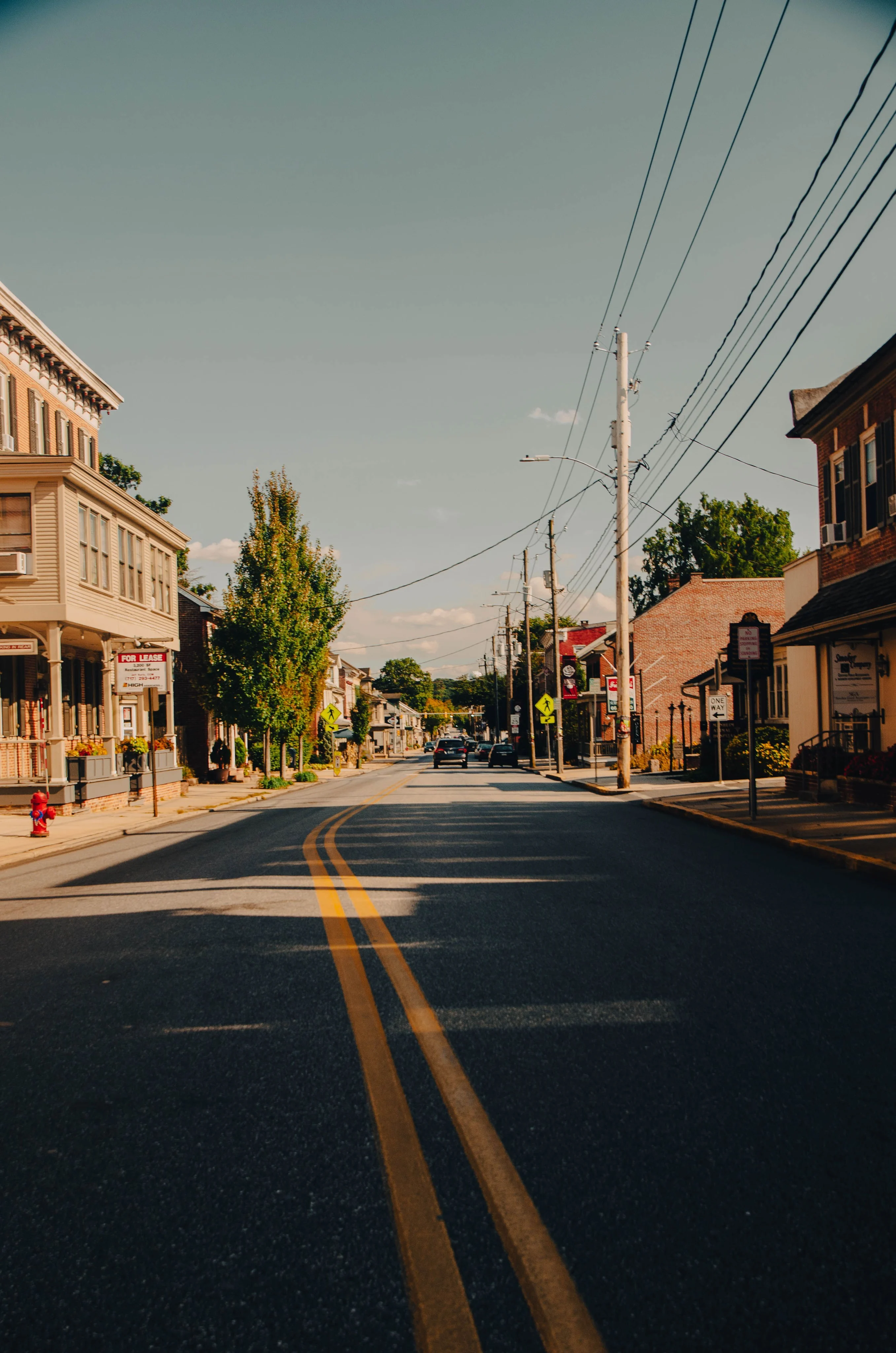 Illustrative small-town main street with storefronts, trees and overhead power lines
