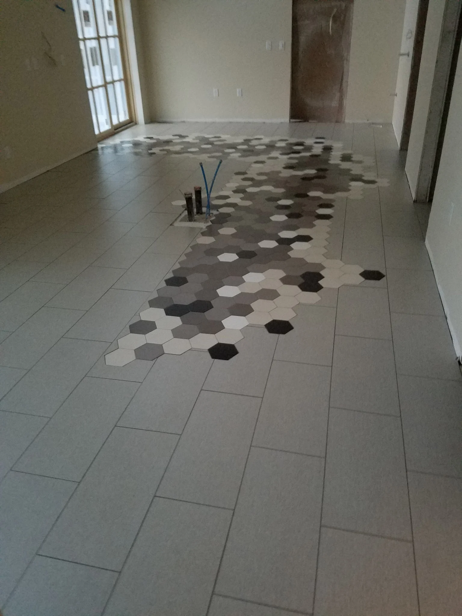 Floor with a flowing band of hexagon tile set into large rectangular tile, mid-install