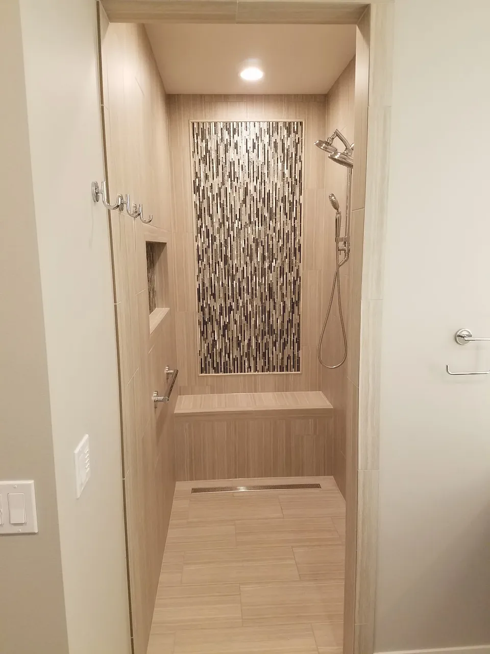 Walk-in shower with a vertical glass mosaic accent panel, tiled bench and linear drain