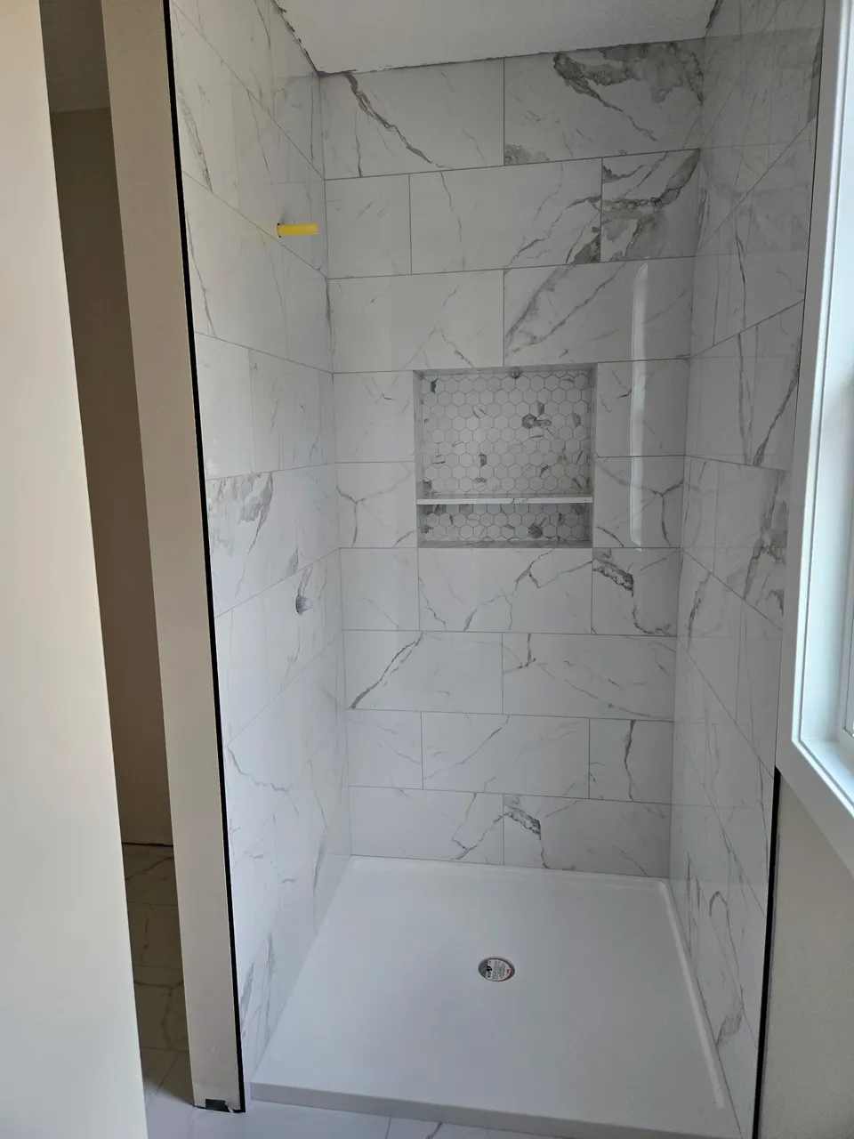 Shower with marble-look wall tile and a hexagon mosaic niche