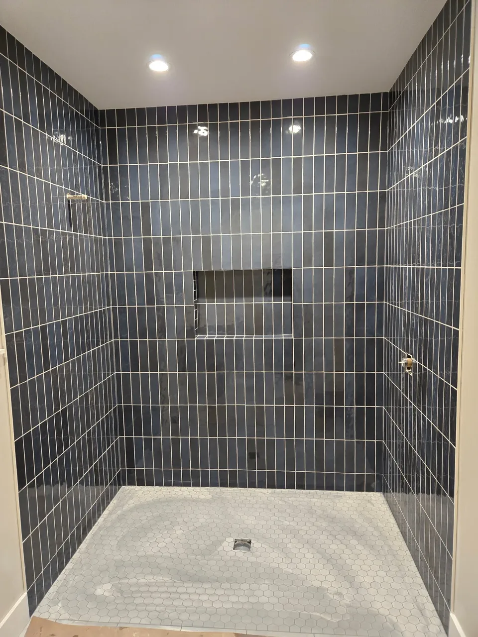 Walk-in shower in dark blue vertical tile with a long recessed niche and hexagon floor