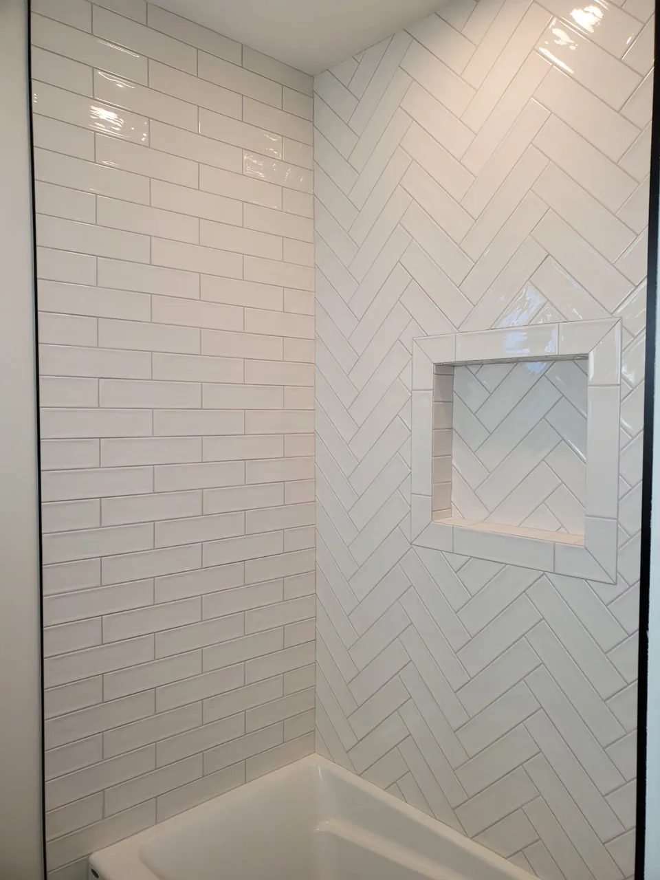 White subway tile shower with a herringbone accent wall and framed niche