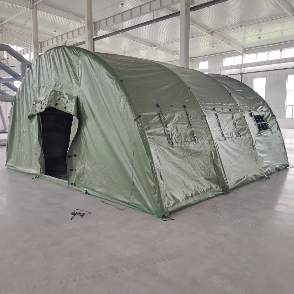 Green high-pressure inflatable tent with an open end entrance and side-window covers in a workshop