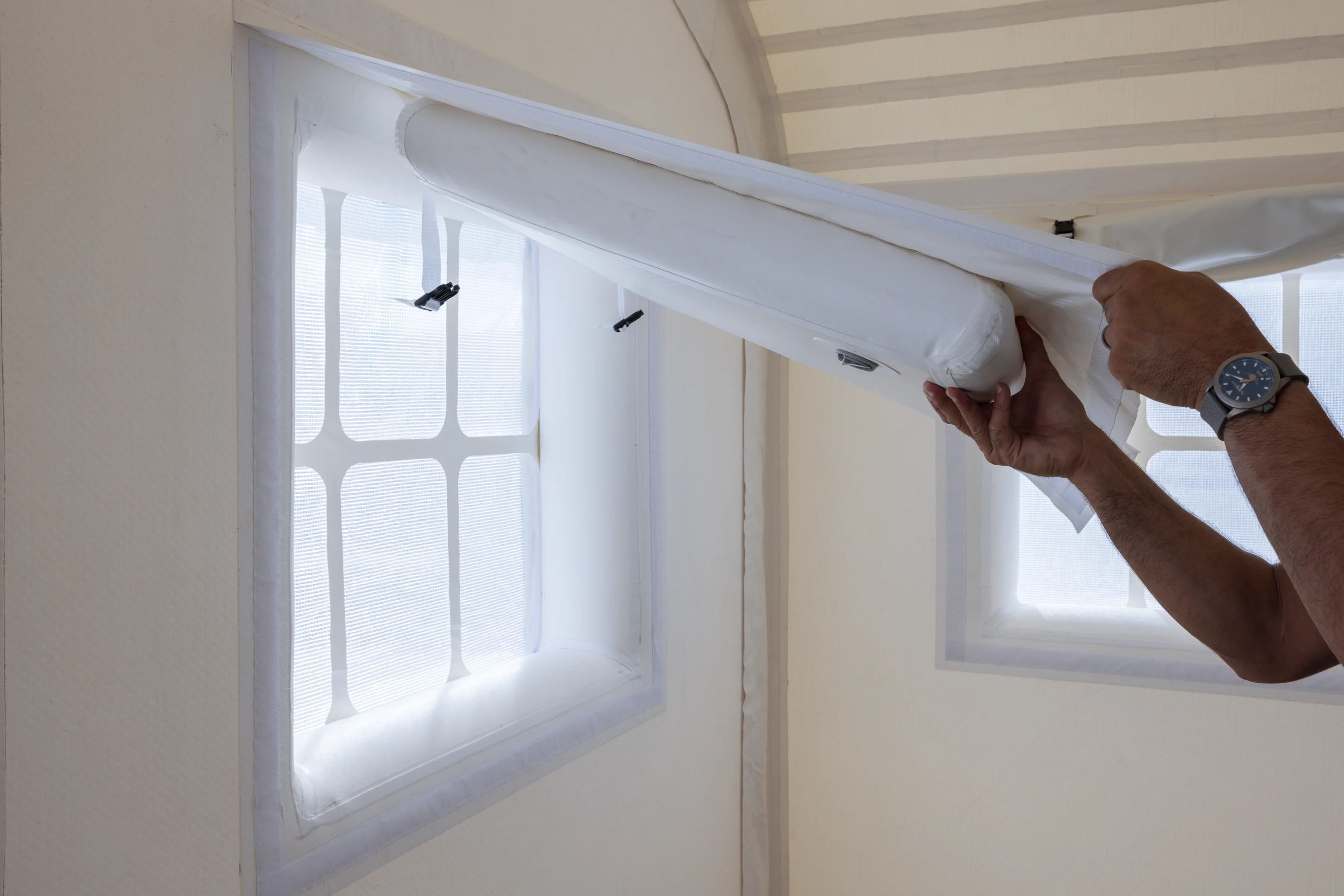Close-up showing a person rolling up the cover of a window inside a white inflatable tent