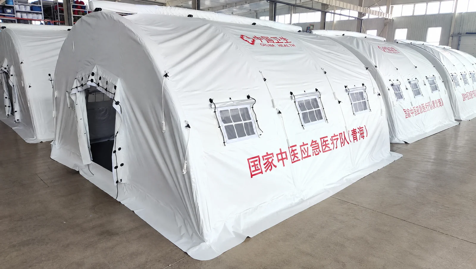 White high-pressure inflatable tents with end entrances, side windows and printed medical markings in a workshop