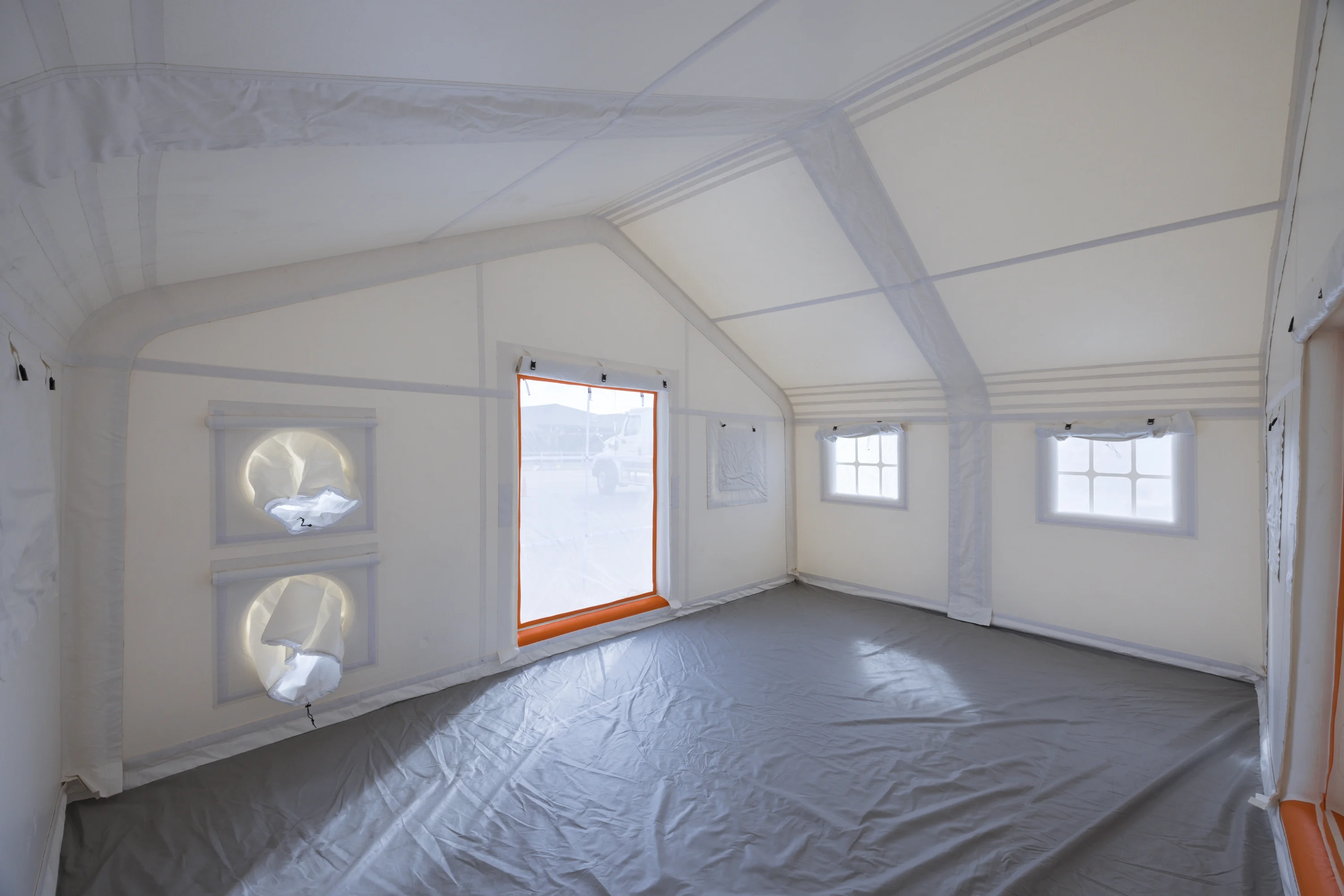Interior of a white drop-stitch inflatable tent with wall panels, roof, windows and gray floor